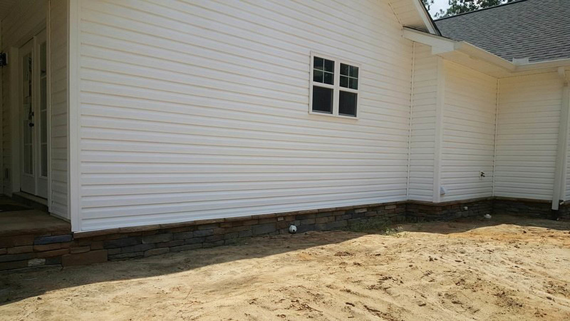 White siding home with rectangular window, brown dirt yard, and football resting near entrance door.
