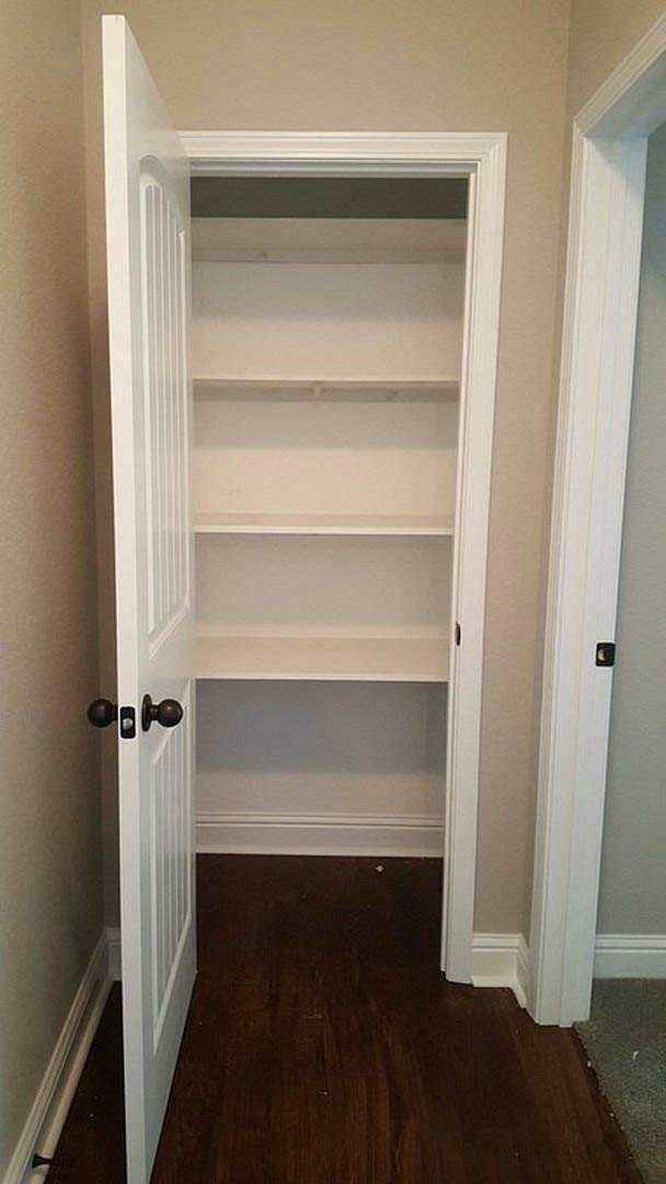 White closet door with silver handle, built-in white shelves, dark hardwood floor, white baseboard trim