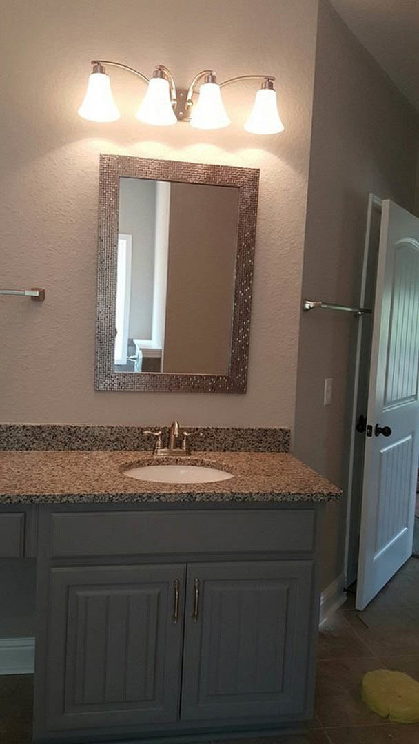 White bathroom with rectangular mirror above a marble countertop, undermount sink, dark wood cabinetry, chrome faucet, and two-bulb wall sconce; yellow soap dispenser sits on the