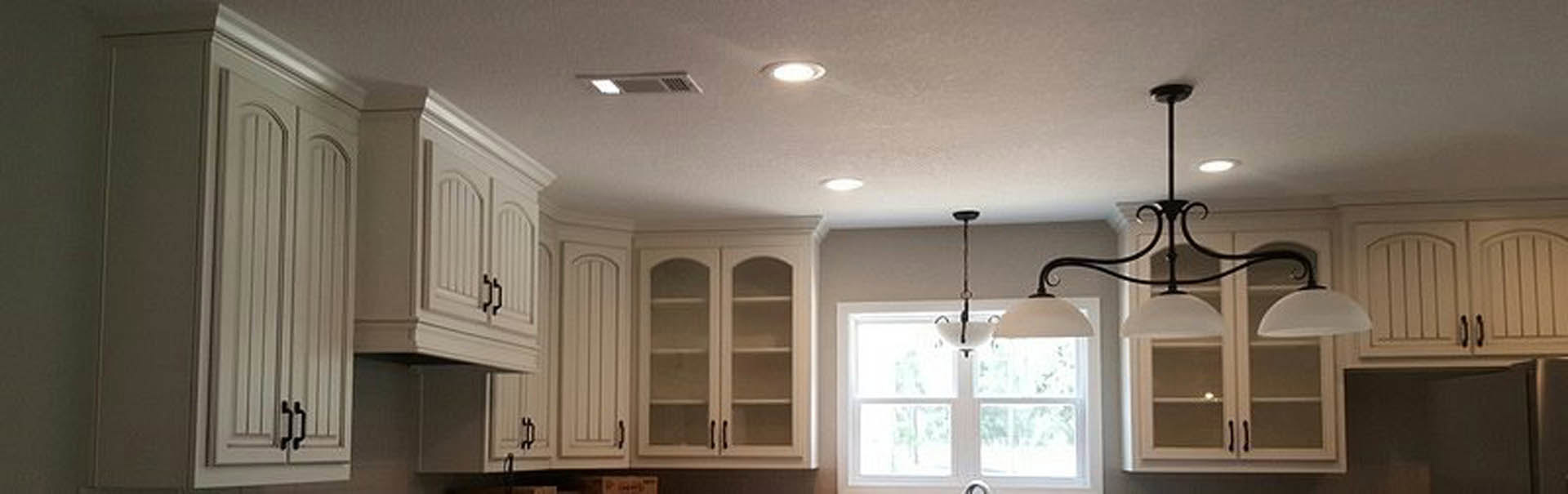 White kitchen cabinets with crown molding, stainless steel appliances, pendant light fixture above island, light gray walls, and hardwood flooring