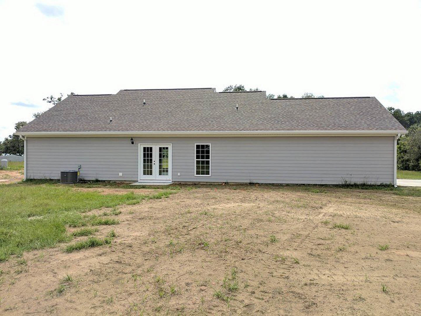 White house with multiple square-paned windows, glass double front door, grassy yard with patches of dirt, blue sky above