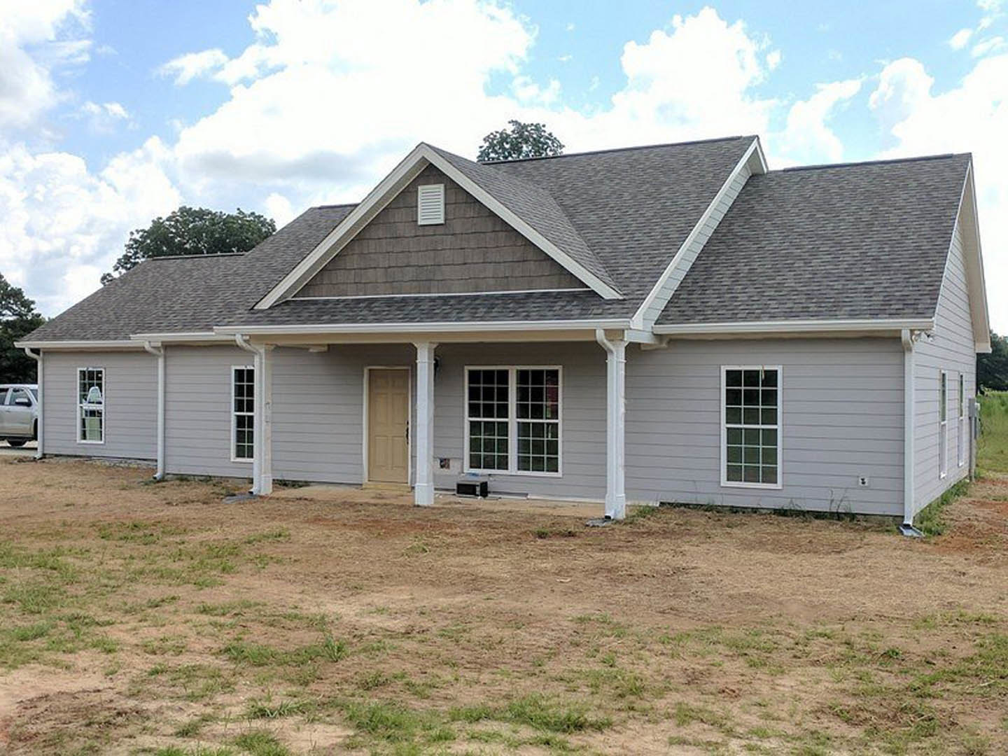 Two-story brick home with white trim, large grassy yard, white framed windows, white front door, and a parked car in the driveway under a cloudy sky