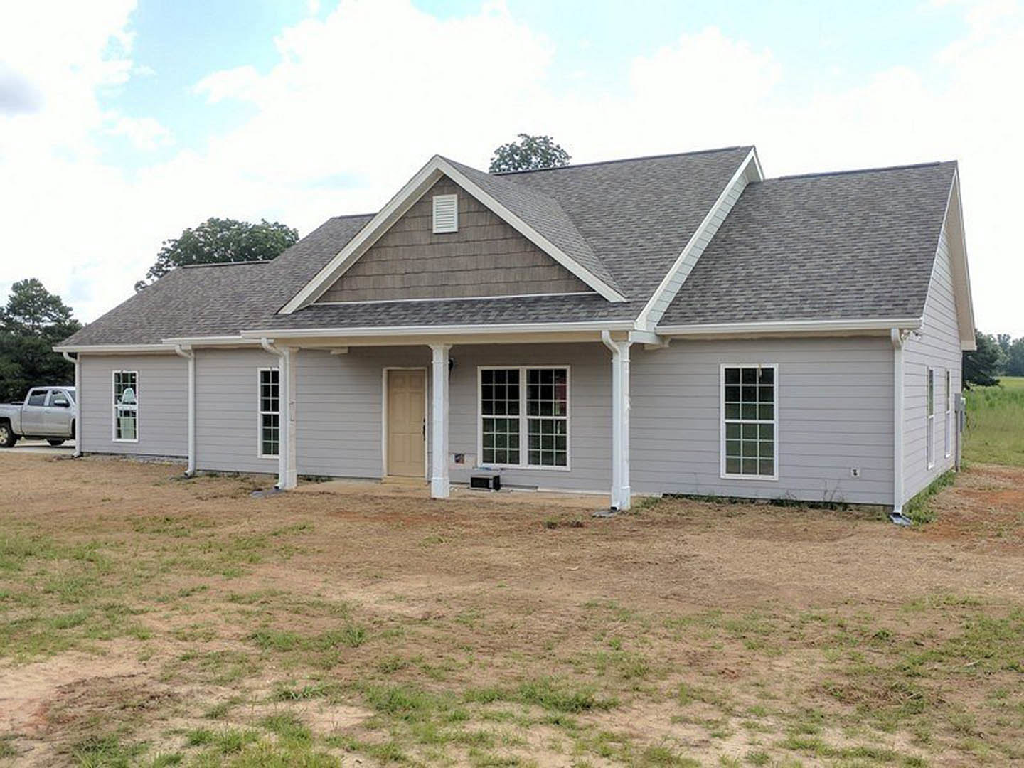 Two-story house with gray roof, white siding, multi-pane windows, black-handled white front door, grassy yard, white truck parked on road, Robert Frost Farm visible in background