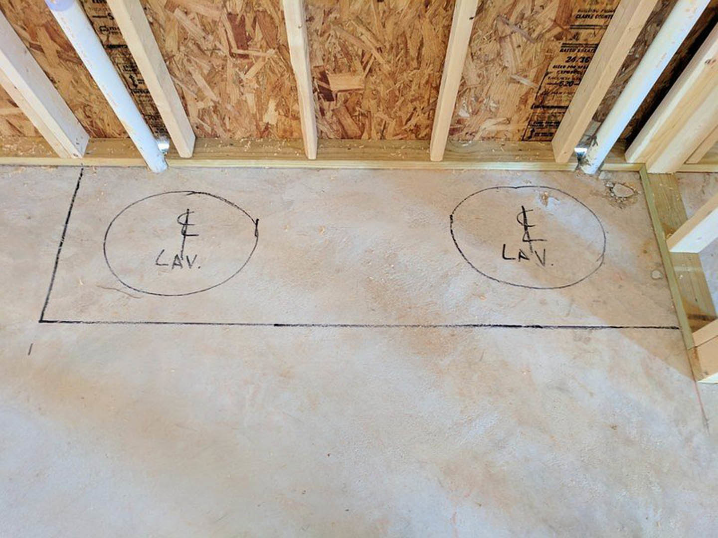 Concrete floor with black circles and lines drawn, adjacent to a beige wall with wood chippings.