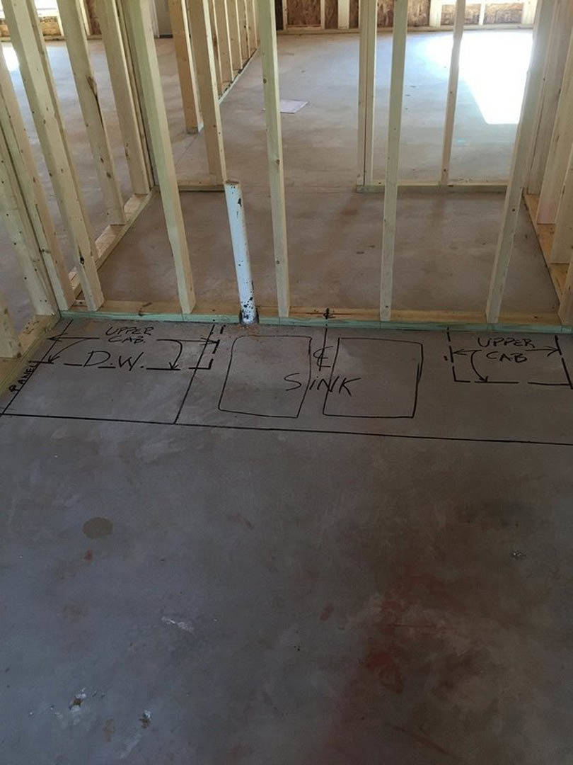 Concrete floor with hand-drawn sink outline in a room featuring exposed wood ceiling beams