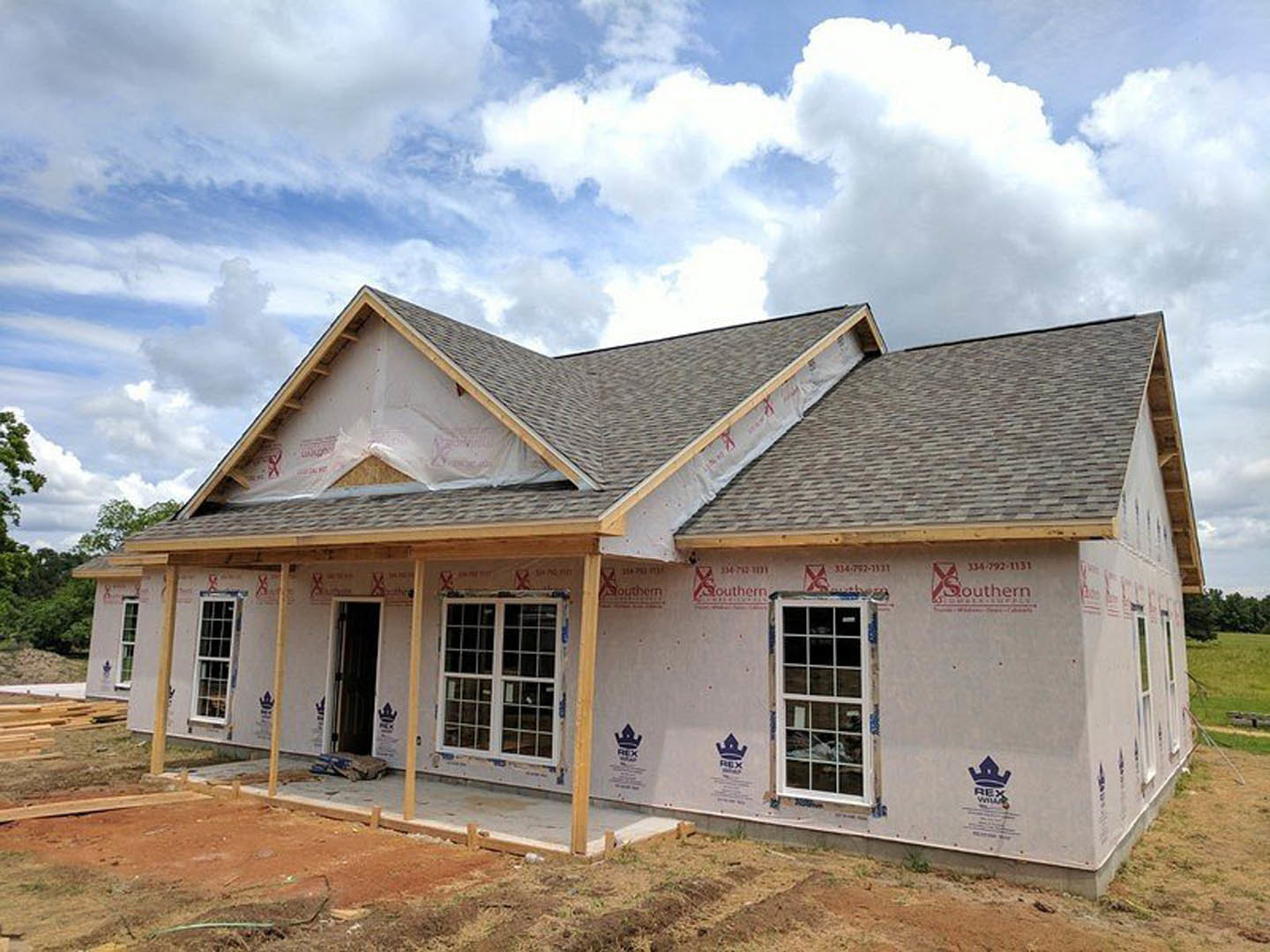 Wood-framed house under construction with unfinished roof, multi-pane windows, and white door, set against clear blue sky