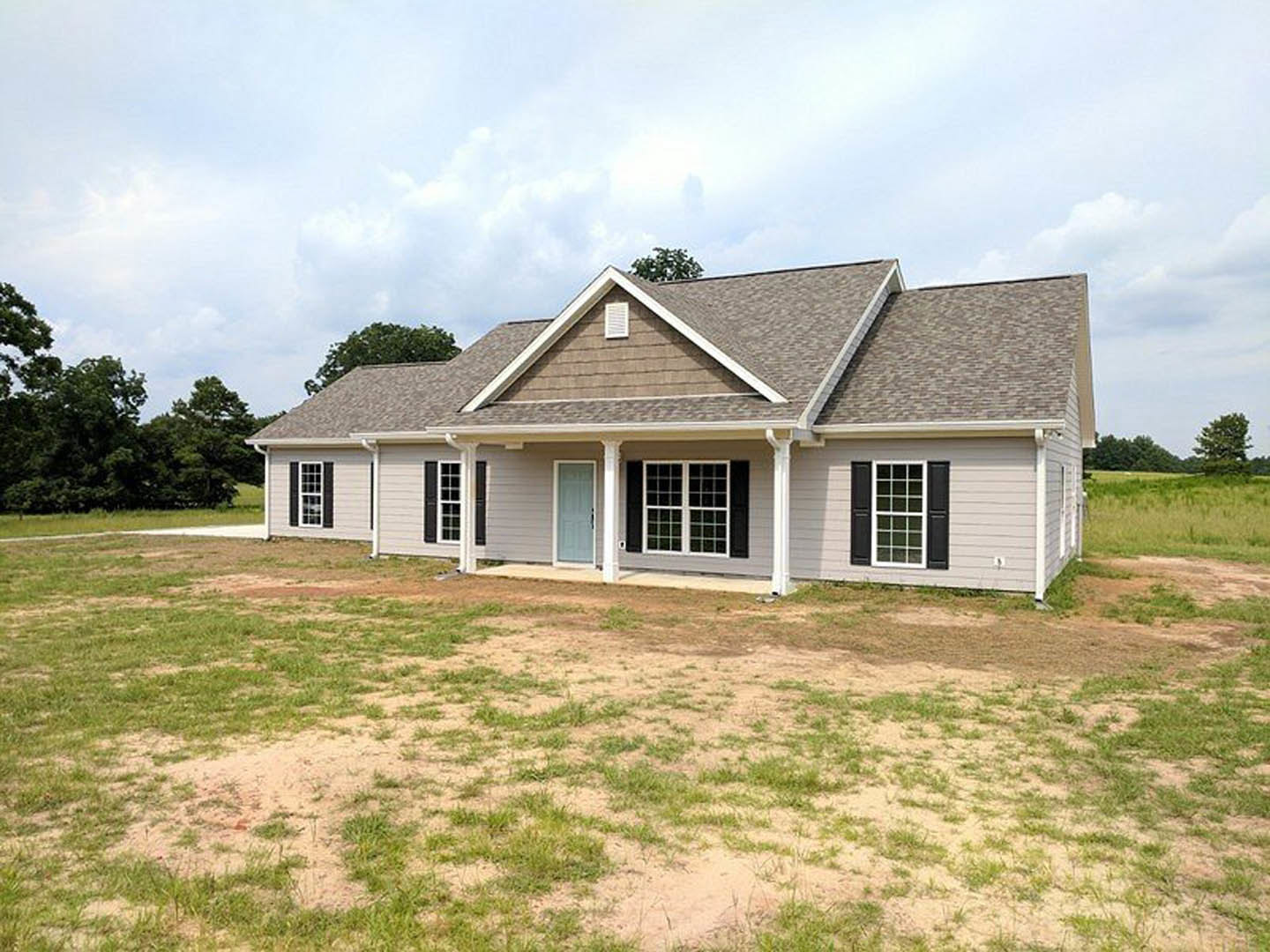 Two-story house with blue door, white columns, black shuttered windows, and white trim, set on a large grassy yard with Robert Frost Farm visible in the background.