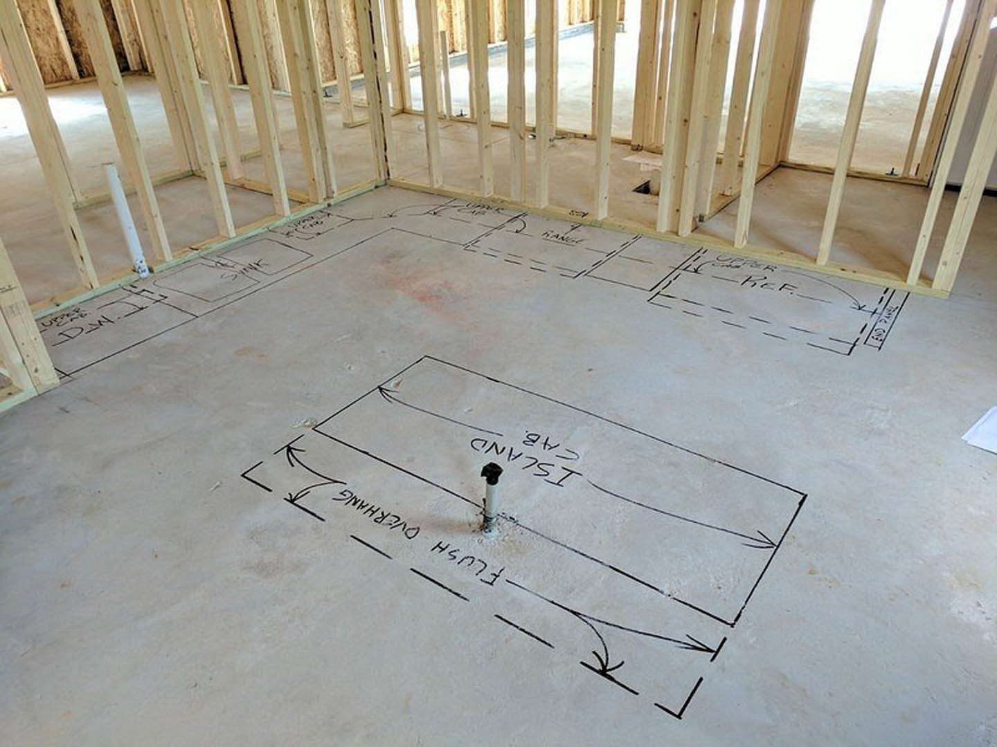 Hand-drawn lines on unfinished concrete floor in a construction zone, wood beam and white cylinder with black top nearby