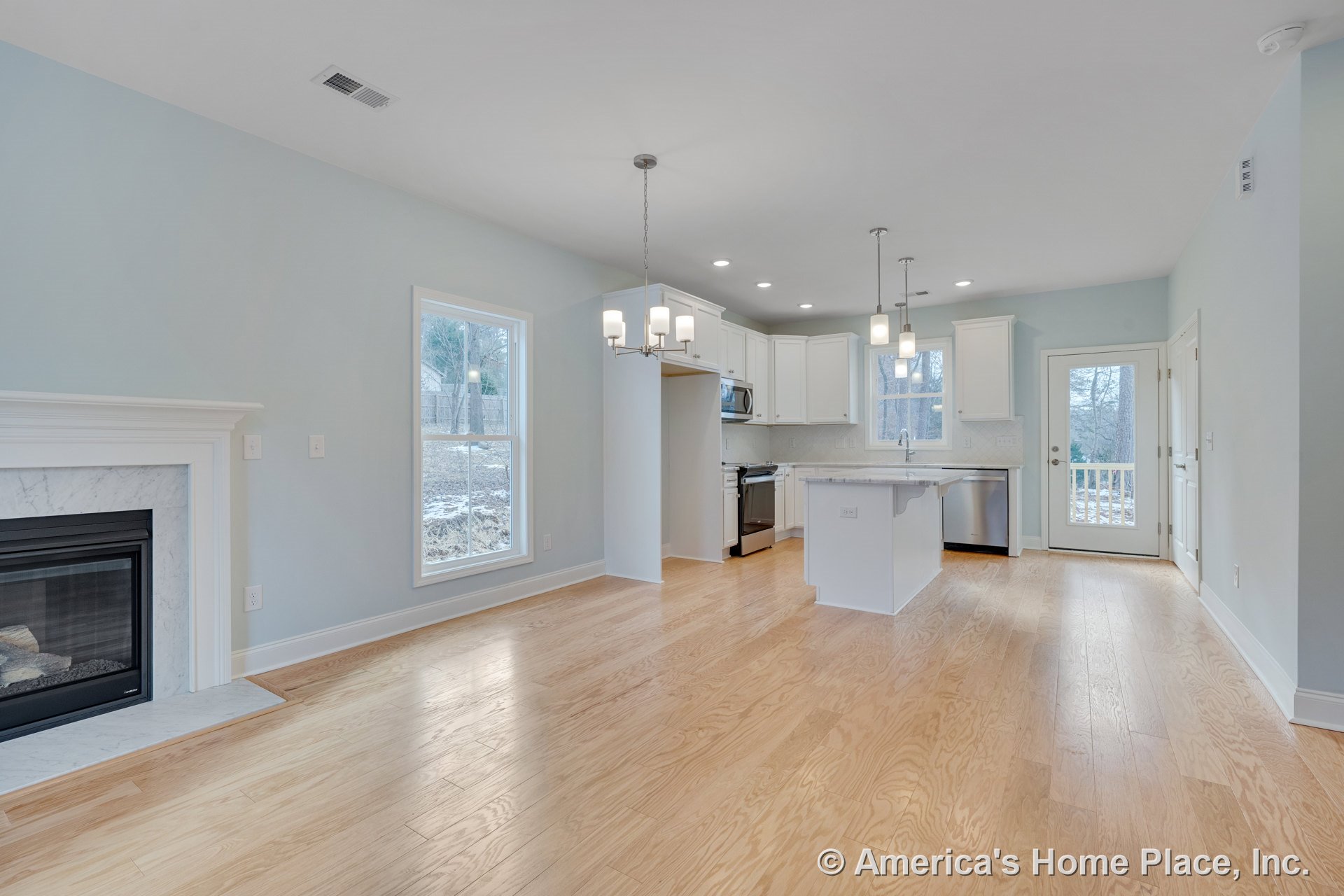 Marble fireplace surround with large double window, hardwood floors throughout open living area, white kitchen cabinets, stone kitchen island countertop, pendant and chandelier