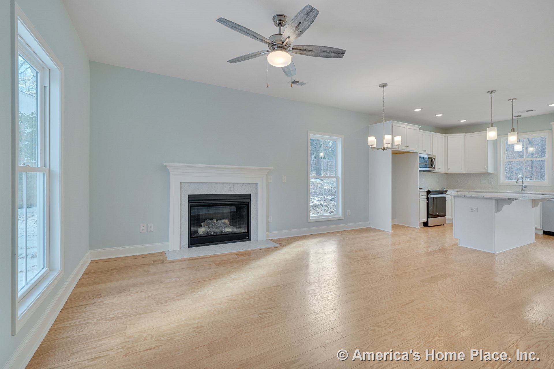 Open floor plan living area with gas fireplace and white mantel, light wood plank flooring, modern kitchen featuring white shaker cabinets and marble countertops, ceiling fan with