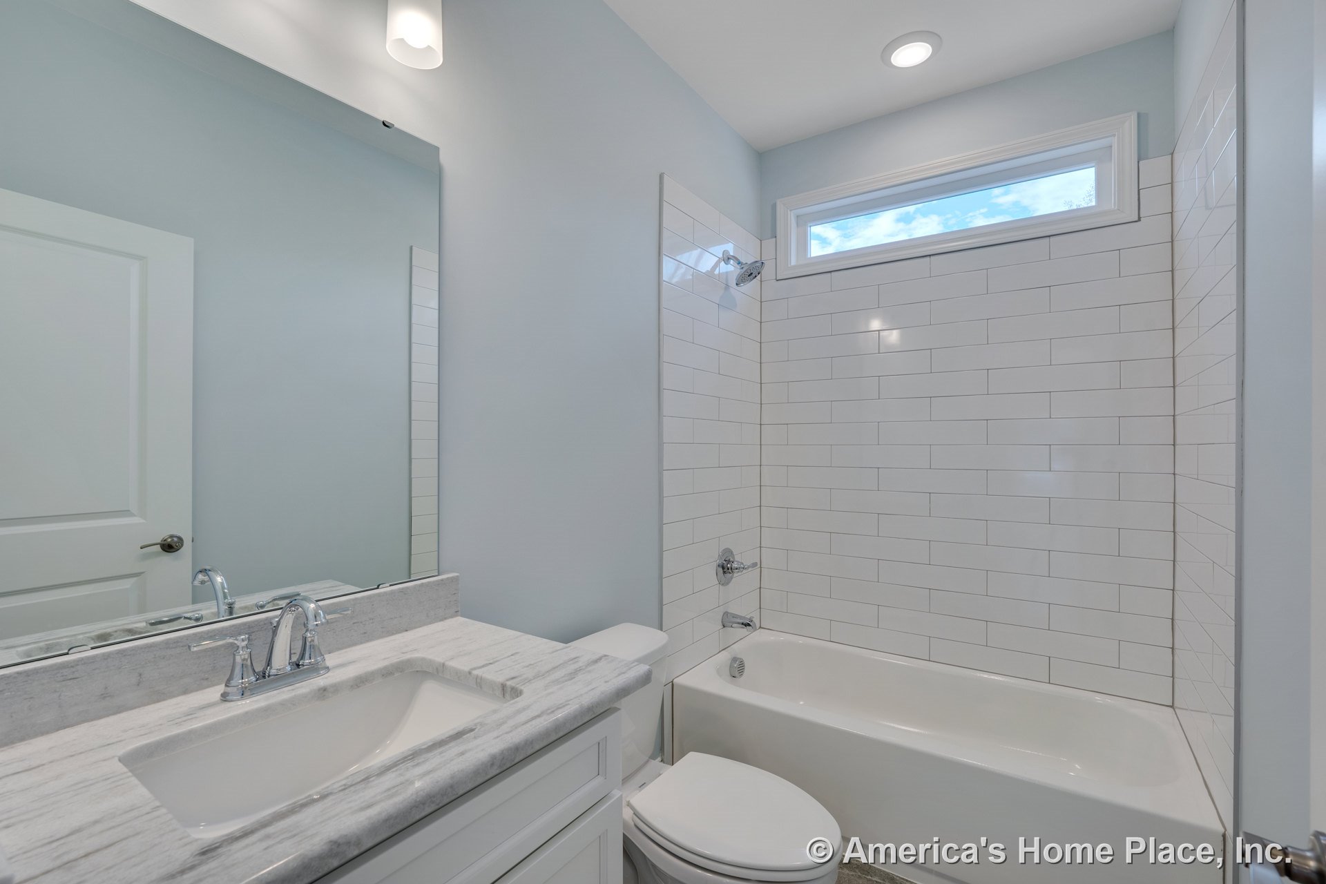 White subway tile shower surround with horizontal window above tub, marble-look vanity countertop with rectangular undermount sink, chrome faucet and fixtures, large wall mirror