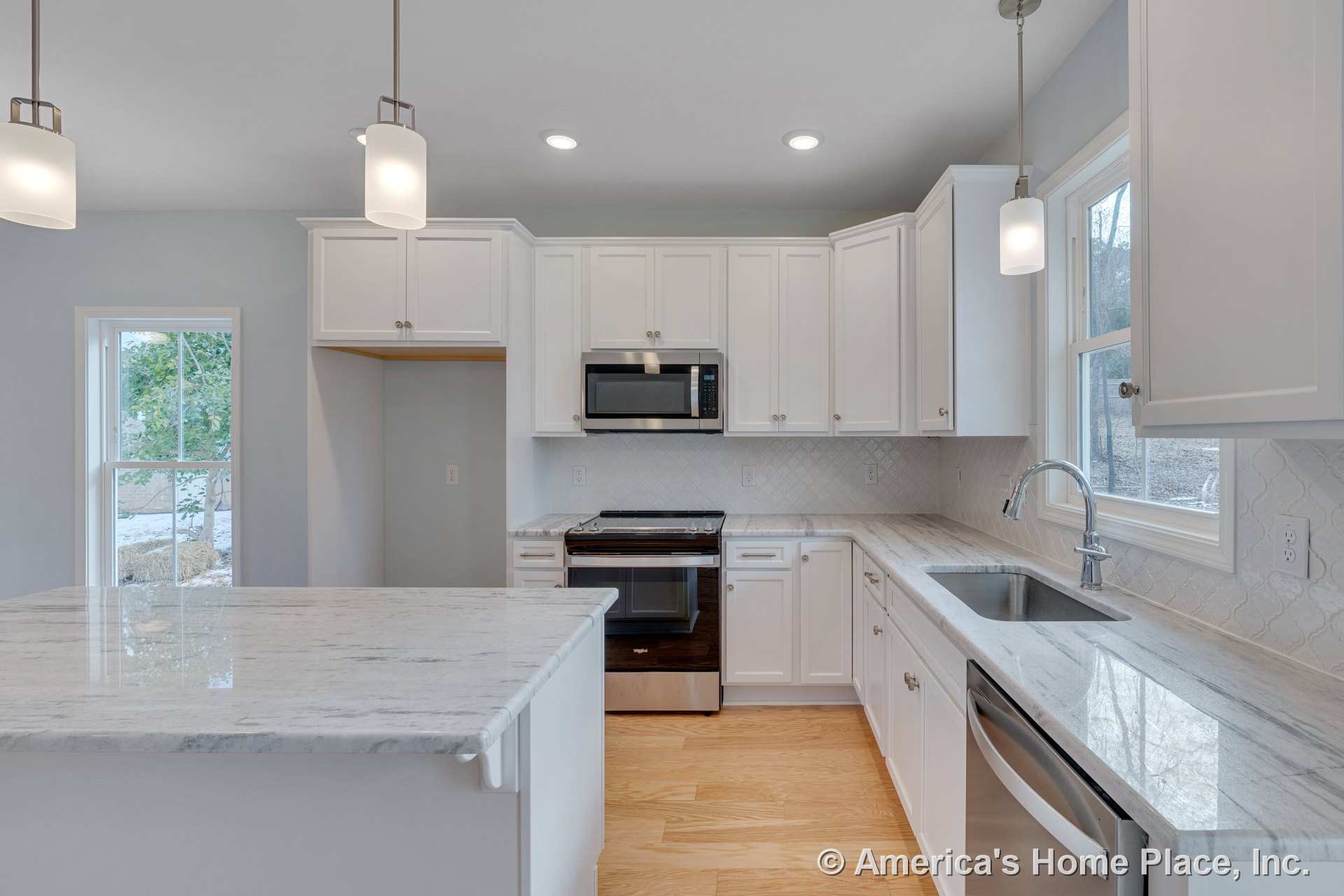 White shaker cabinets and marble island countertop with stainless steel oven, built-in microwave, tile backsplash, single bowl sink beneath window, pendant and recessed lighting