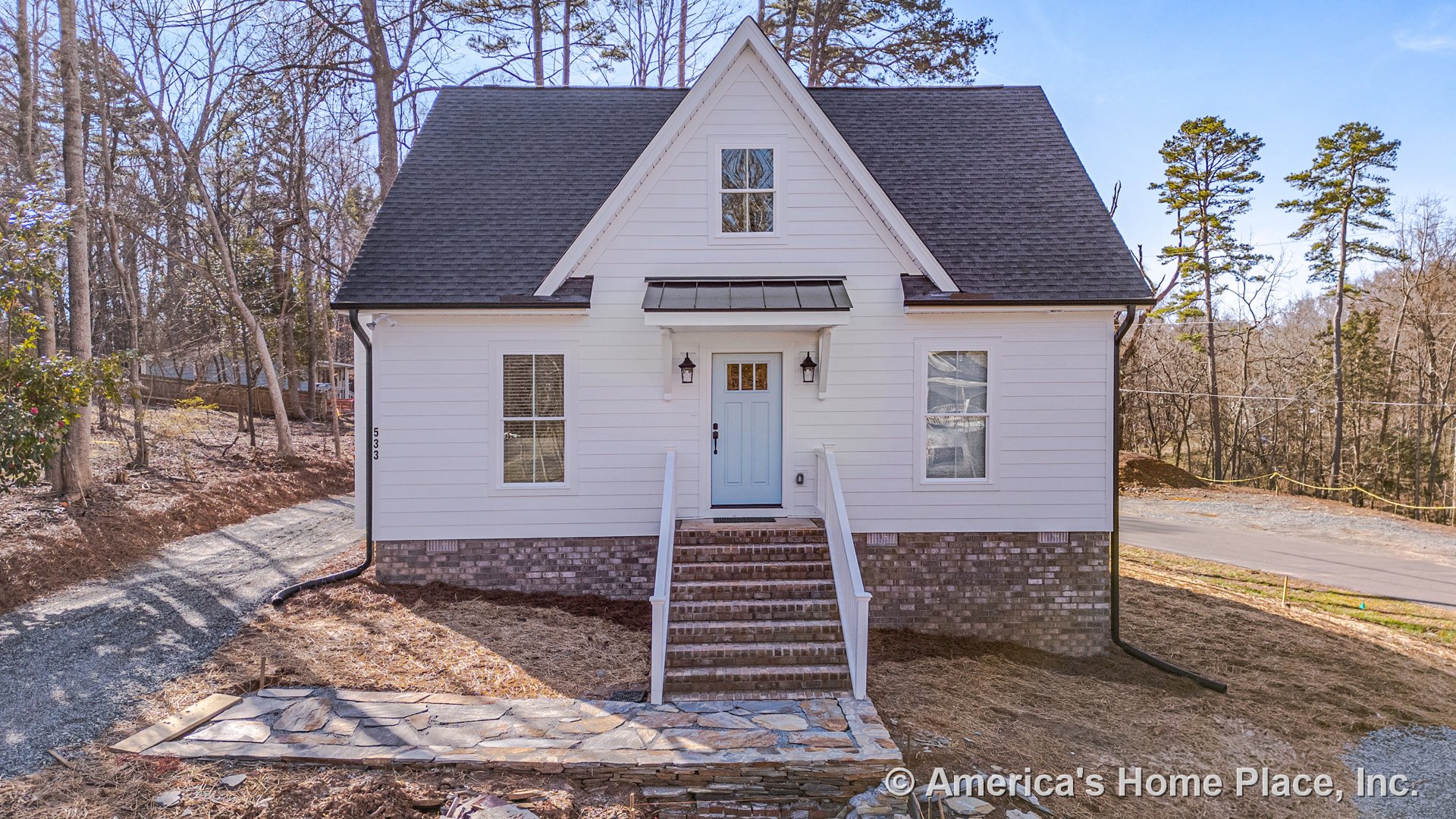 White horizontal siding and brick foundation with gabled roof featuring architectural shingles; front porch with brick steps, double hung windows, metal awning above entry door