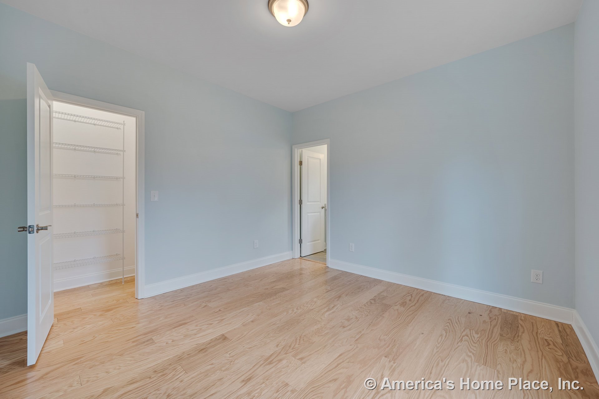 Bedroom with light wood flooring, pale blue walls, white baseboards, built-in closet featuring wire shelving, flush mount ceiling light, and white paneled doors.