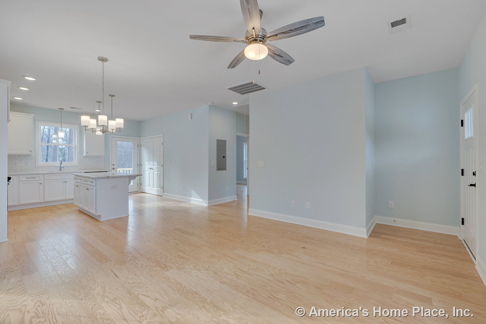 Open floor plan with light wood flooring, white kitchen cabinetry, central kitchen island, ceiling fan with light, pendant chandelier, recessed lighting, double doors leading