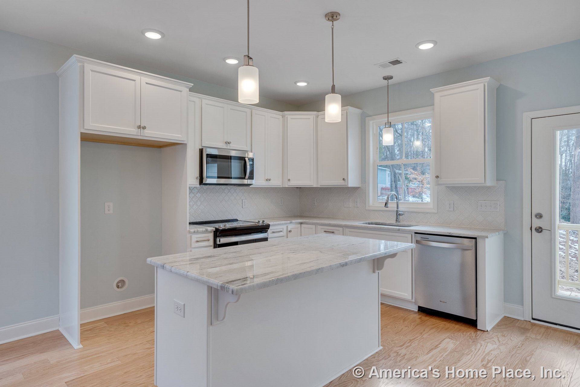 White upper and lower cabinets, marble island countertop, stainless steel dishwasher, built-in microwave above stove, tile backsplash, pendant and recessed ceiling lights, window