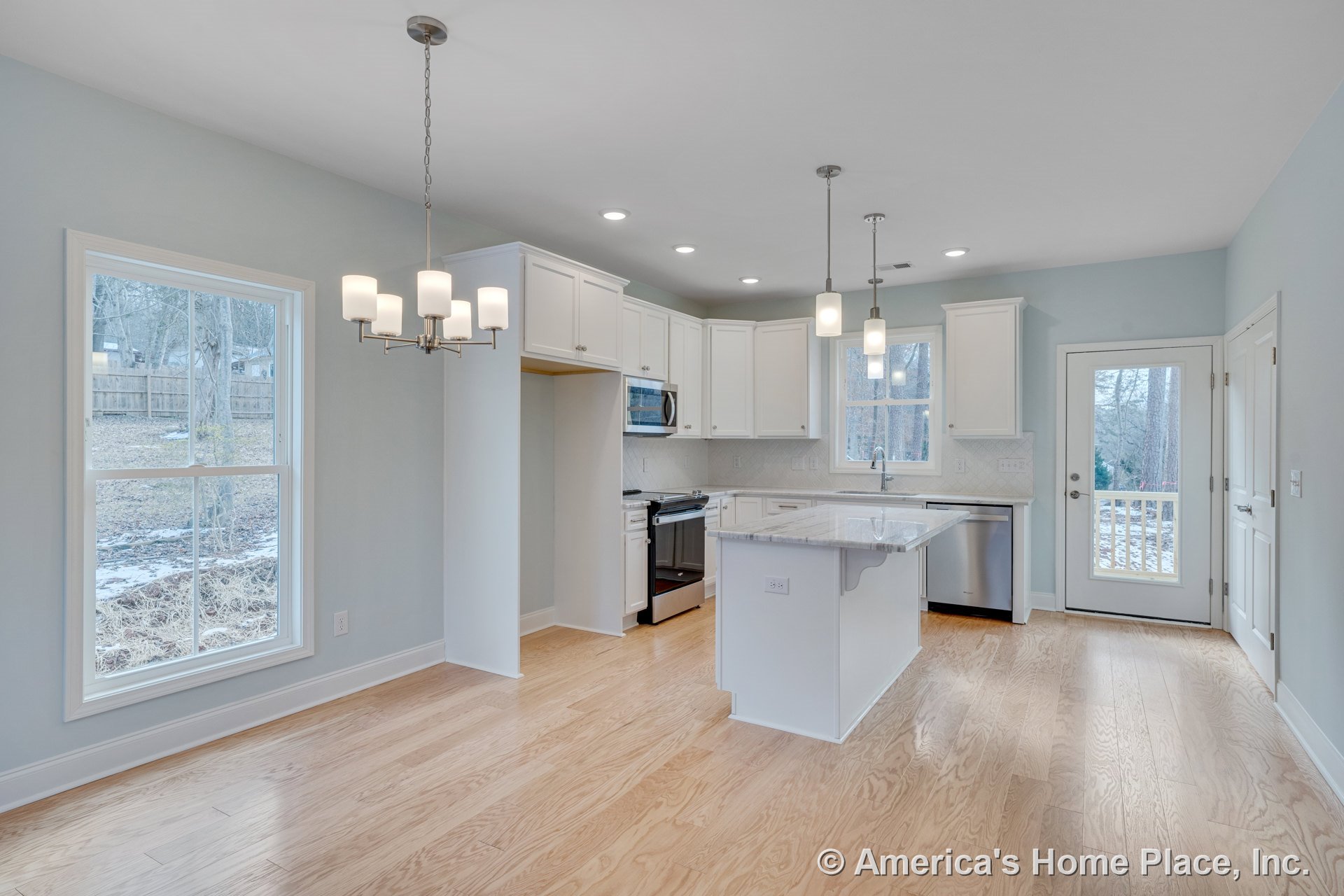 White shaker cabinets and marble kitchen island with stainless steel appliances, pendant lights above the island, hardwood flooring, large windows, built-in microwave, adjacent