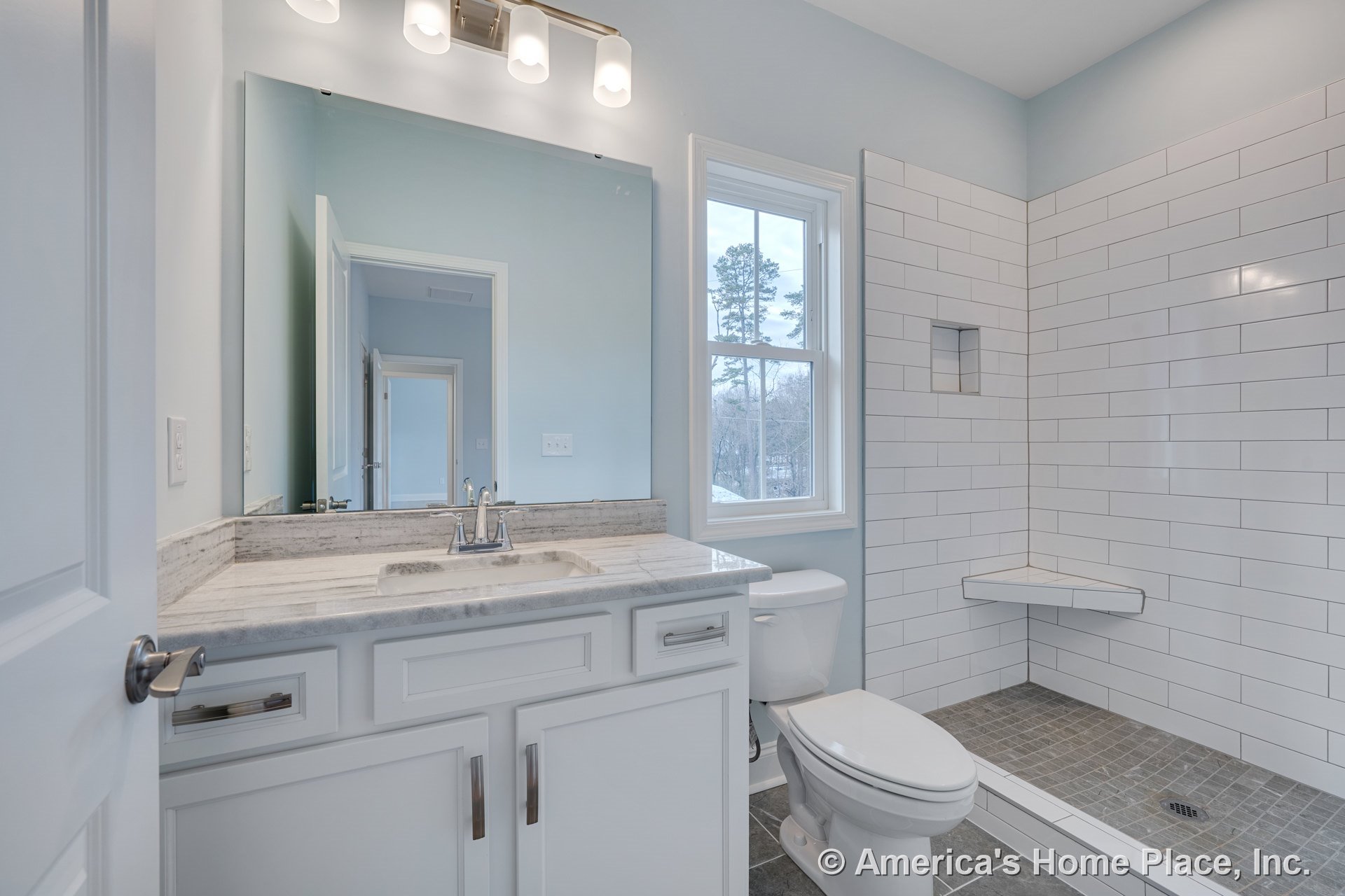 Walk-in shower with white subway tile, built-in corner bench, gray tile floor, marble countertop vanity with white shaker cabinets, large wall mirror, three-light fixture above