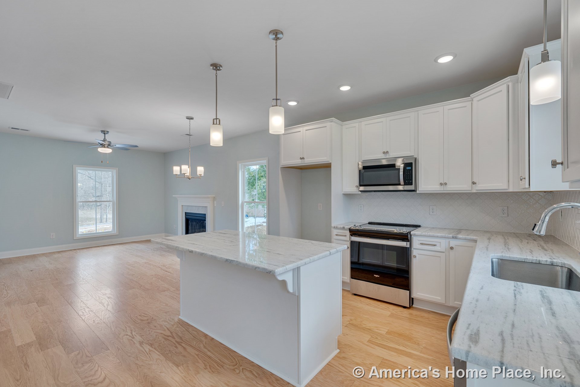 White shaker kitchen cabinets, marble island with stainless steel oven and microwave, pendant and recessed lighting, light wood flooring, open layout leading to living room with