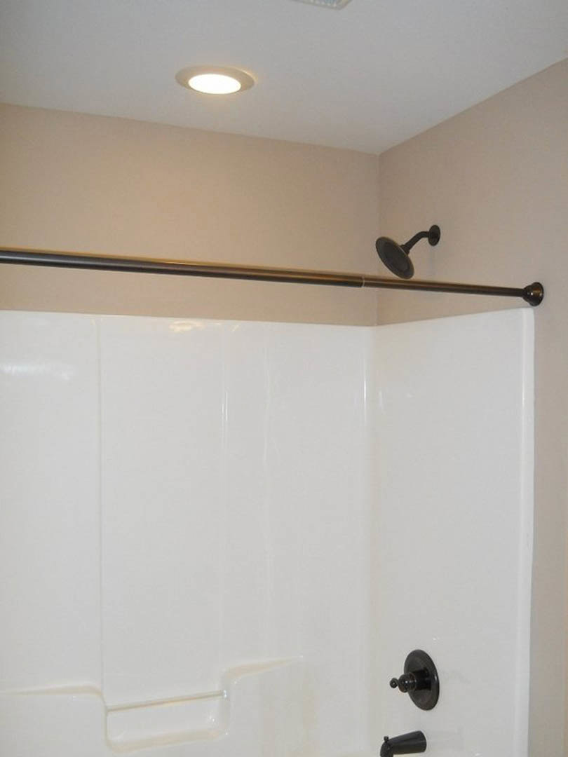 White shower with black fixtures, chrome shower head, curved metal shower rod, recessed ceiling light, close-up of wall hook, black round wall accent