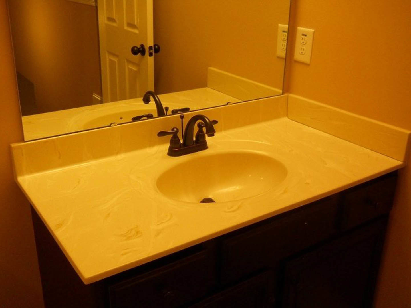 White ceramic sink with chrome faucet beneath a rectangular mirror, set against light-colored tile wall with visible electrical outlet.