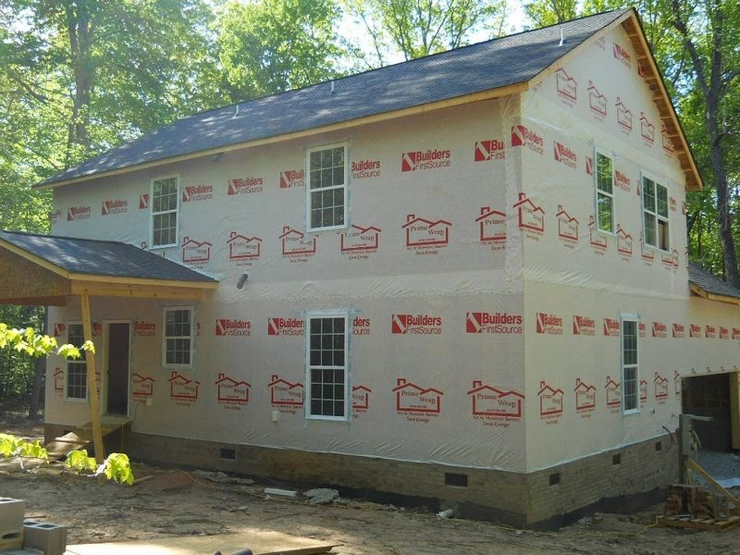 Two-story house with gray siding, covered front porch supported by white columns, white-framed windows, dark shingle roof, landscaped yard with green grass and trees