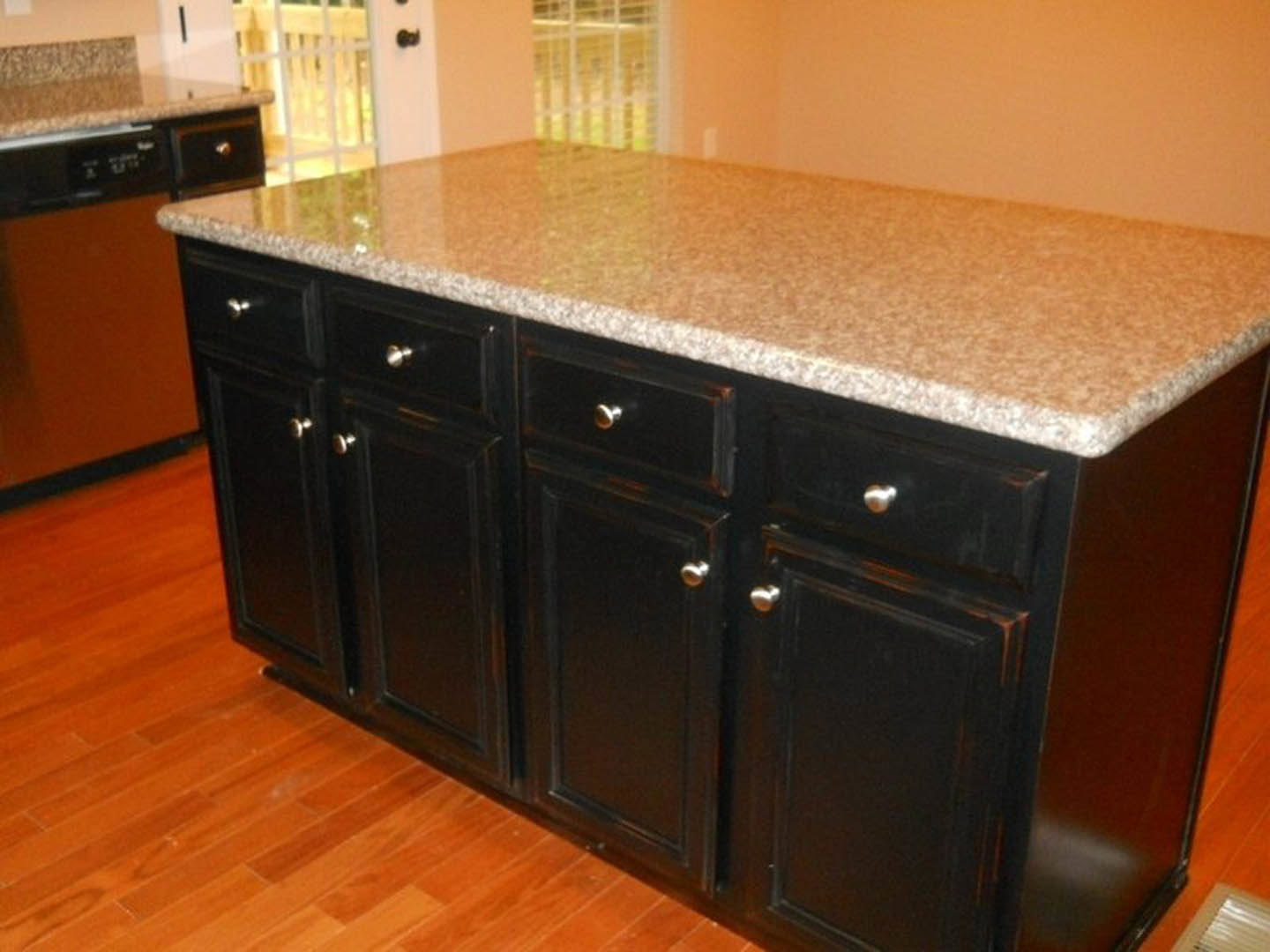 Granite kitchen island with white cabinetry, stainless steel appliances, wood flooring, and drawers visible