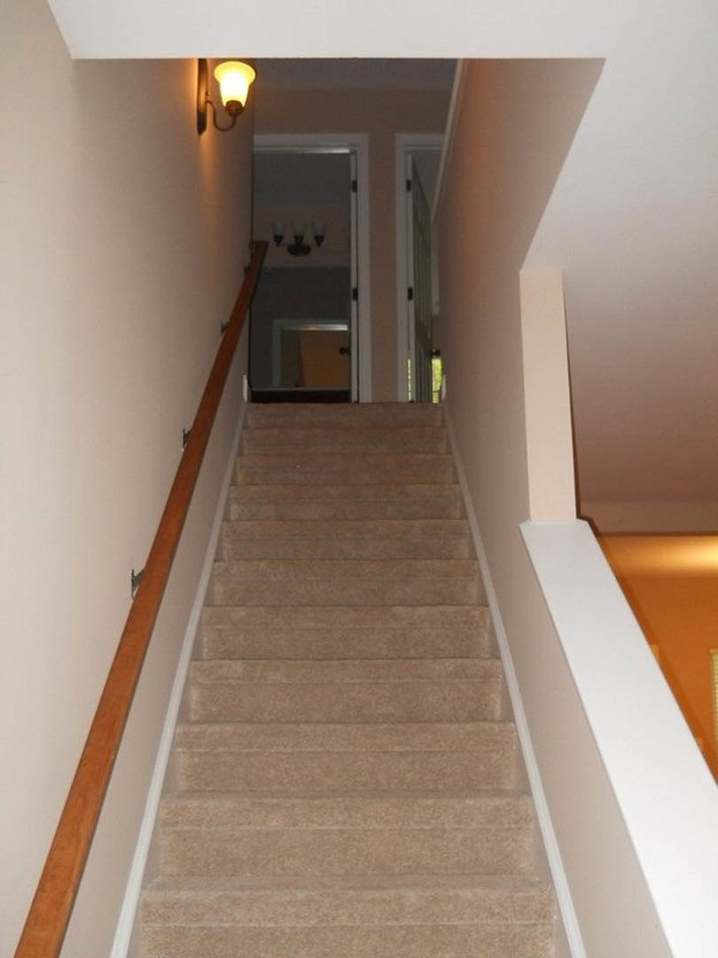 Wood staircase with metal handrail, plaster walls, modern wall-mounted light fixture, hardwood flooring, and white ceiling.
