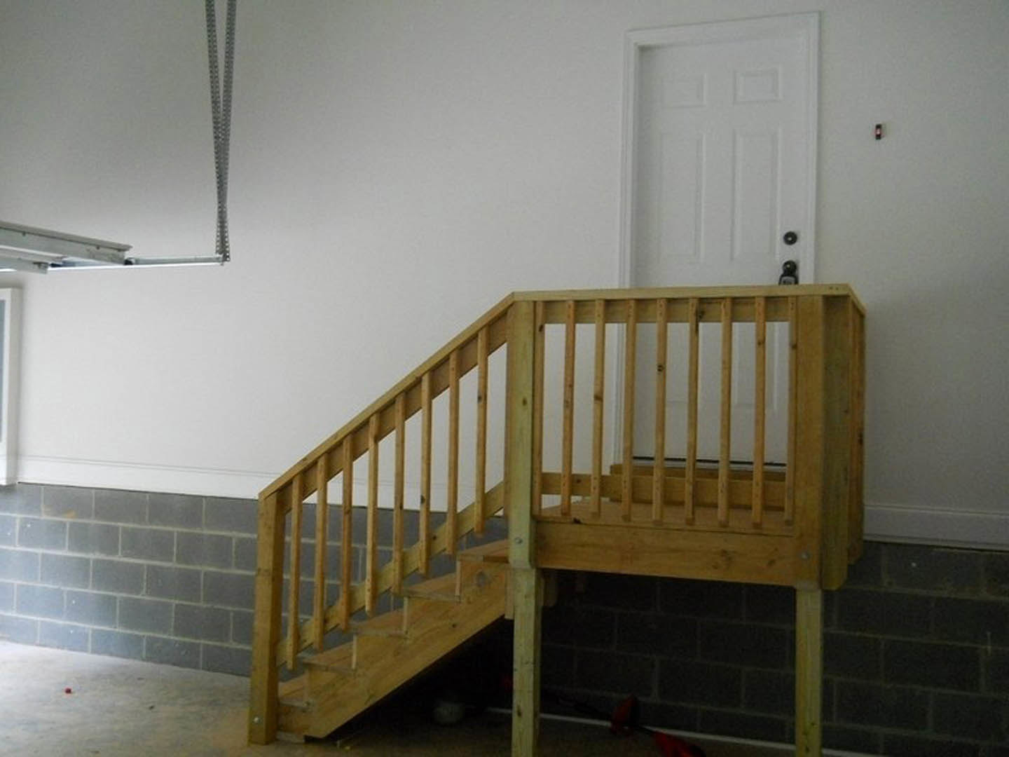 Wooden staircase with metal handrail beside exposed brick wall, white door, and plaster walls in modern indoor room