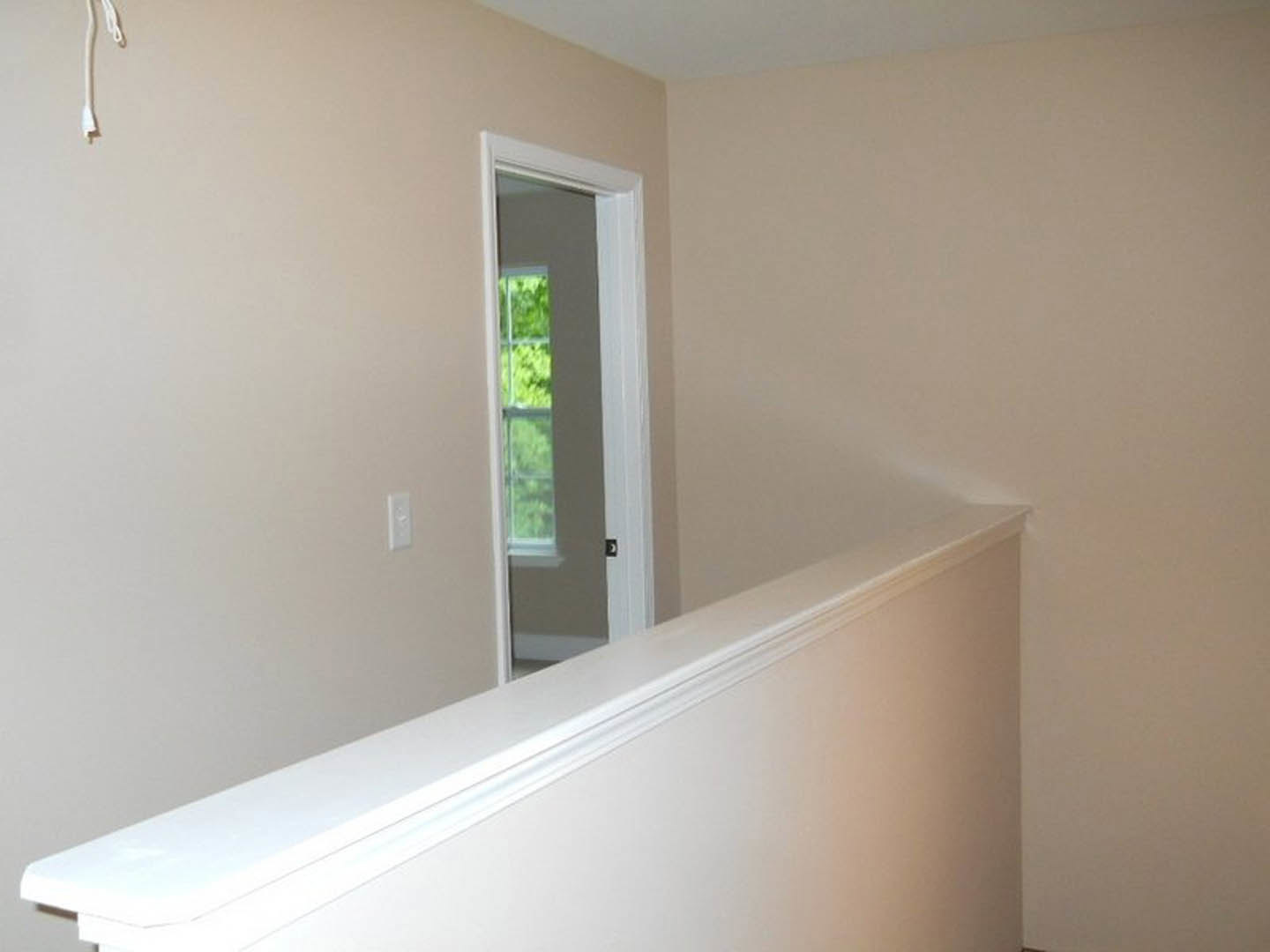 Hallway with white painted railing, smooth plaster walls, open doorway, and large window letting in natural light