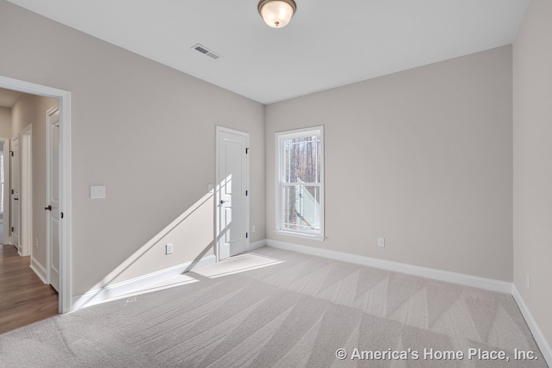 Bedroom with light beige carpet, neutral walls, white trim and baseboards, double panel interior doors, large divided-light window, flush mount ceiling fixture, and modern