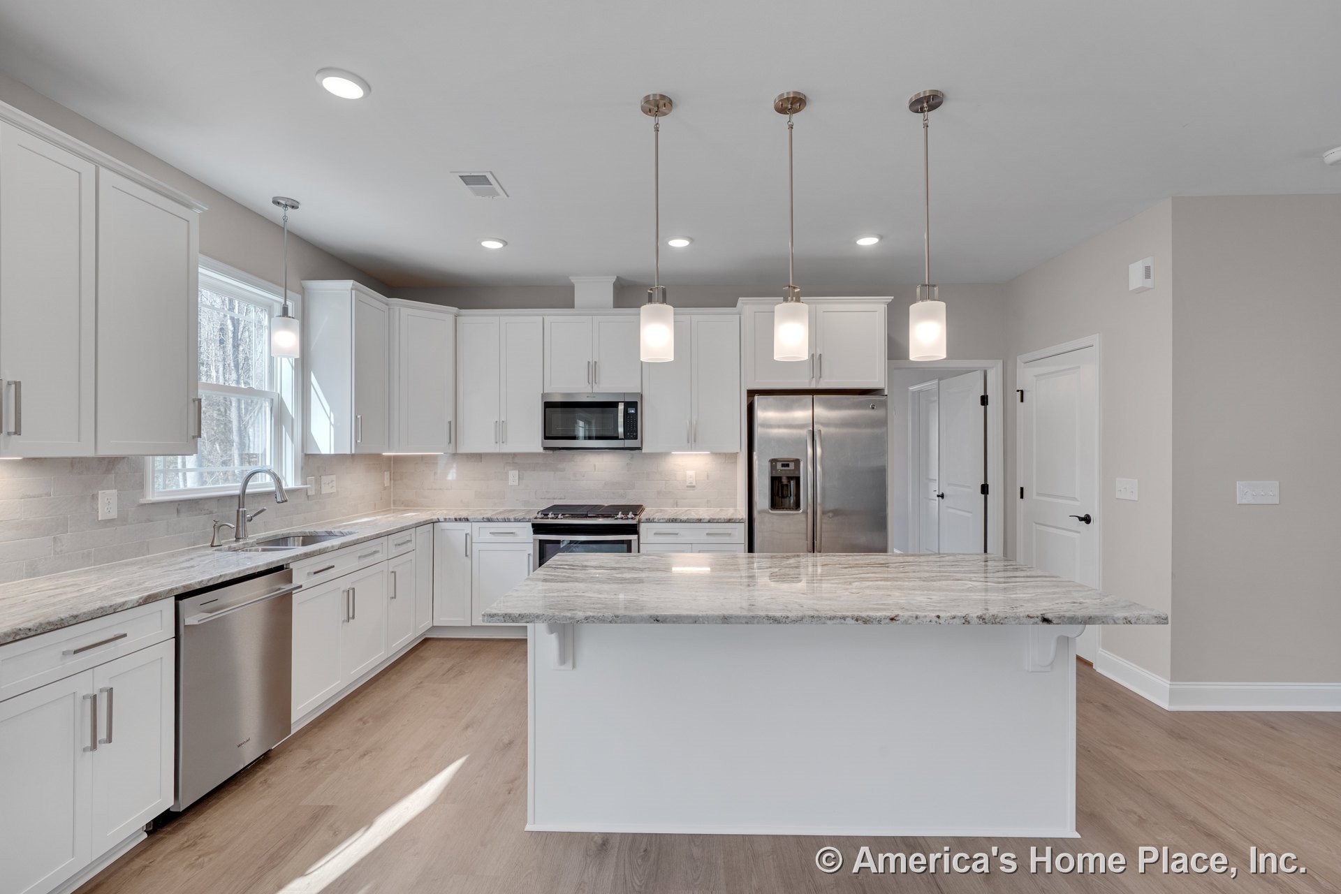 White kitchen with granite countertops, large central island, pendant lighting, subway tile backsplash, stainless steel double-door refrigerator, built-in microwave, wide window