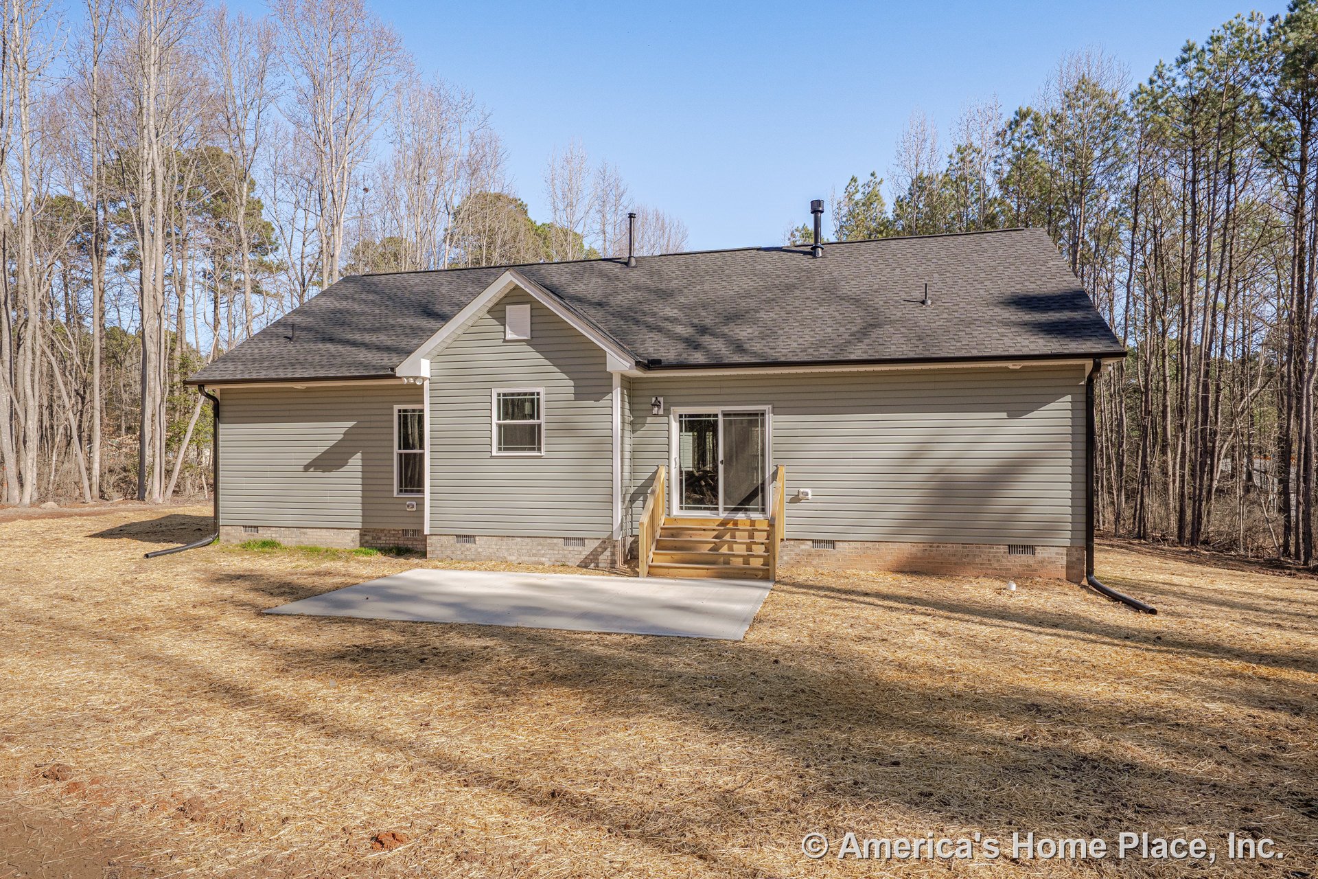 Gray vinyl siding exterior with gable roof, rear entry featuring wooden steps, sliding glass door, concrete patio, brick foundation, white trim, multiple windows, and outdoor