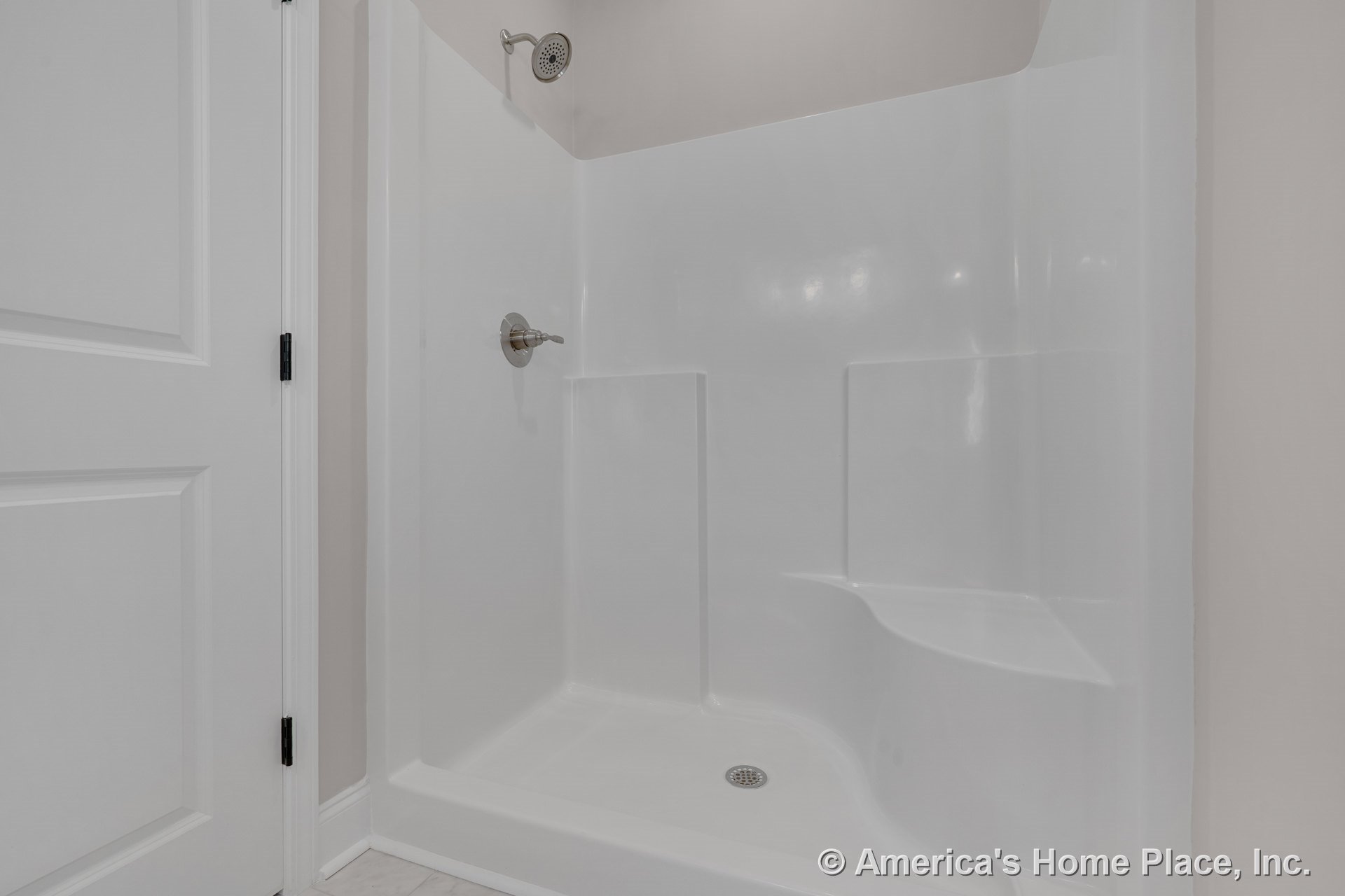 Fiberglass shower enclosure with molded seat, chrome showerhead and faucet handle, white paneled door, tile flooring, minimalist built-in fixtures.