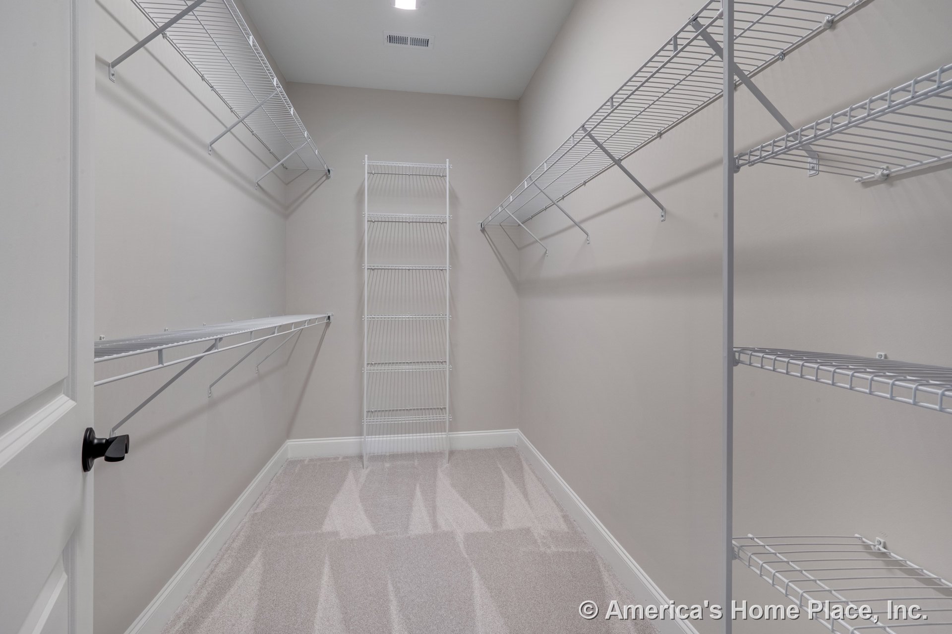 Walk-in closet with built-in white wire shelving, carpeted floor, neutral painted walls, baseboard trim, recessed ceiling light, closet door with lever handle, and ceiling vent.