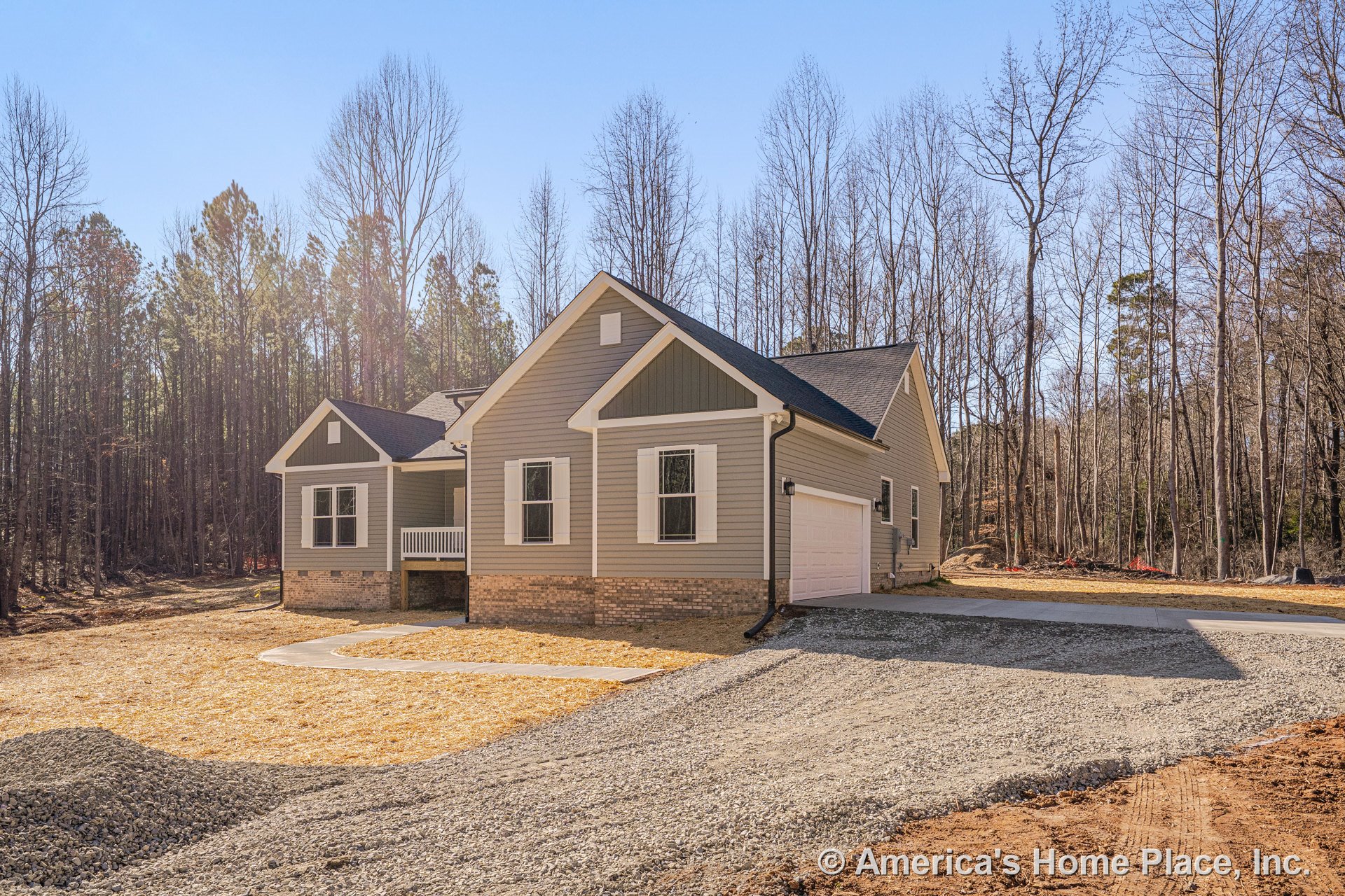 Two-car attached garage with brick foundation, vinyl siding exterior, white window trim, covered front porch, gabled roof, and paved driveway.