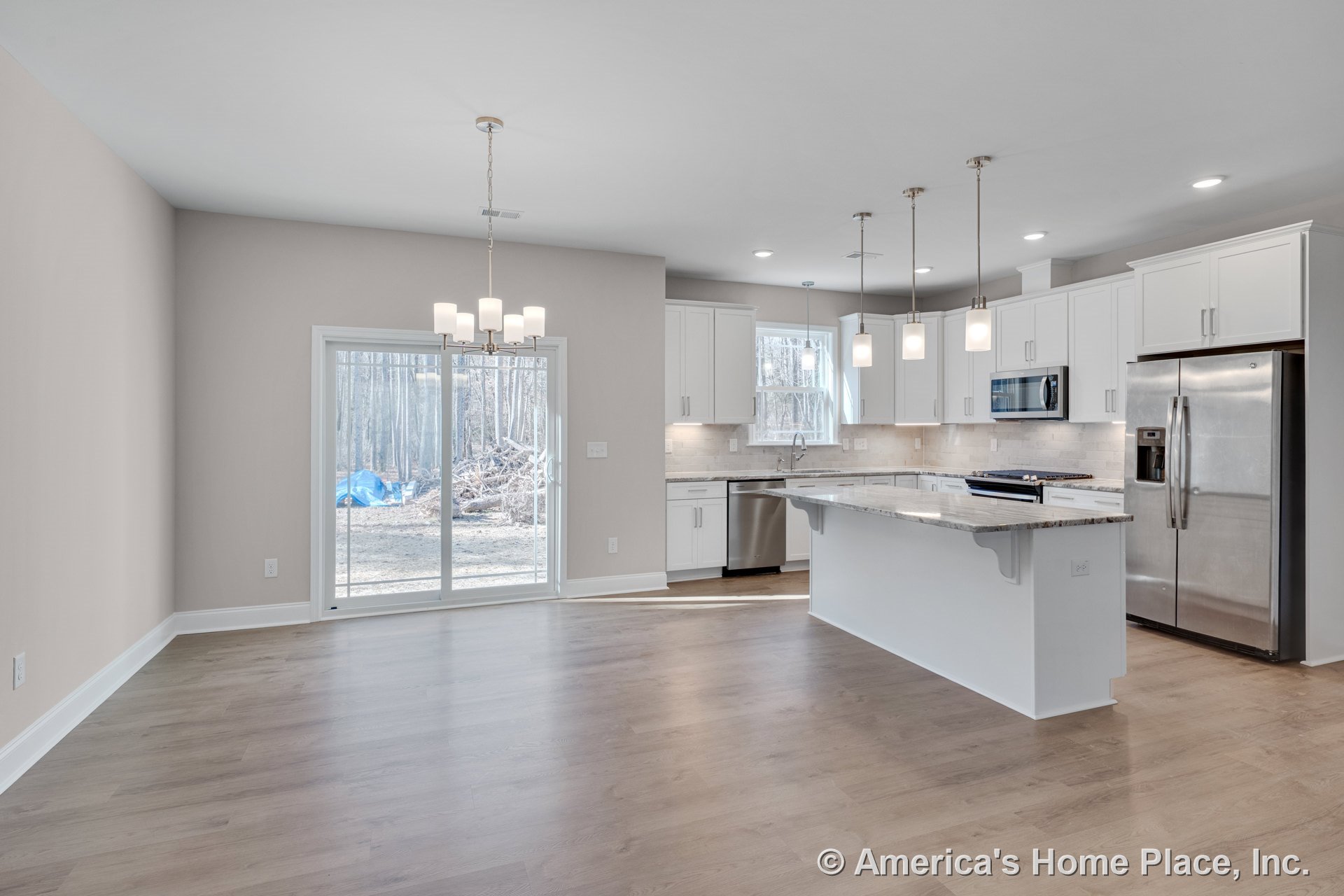 Open kitchen with white shaker cabinets, granite countertops, large central island with multiple pendant lights, built-in stainless steel refrigerator, microwave, dishwasher