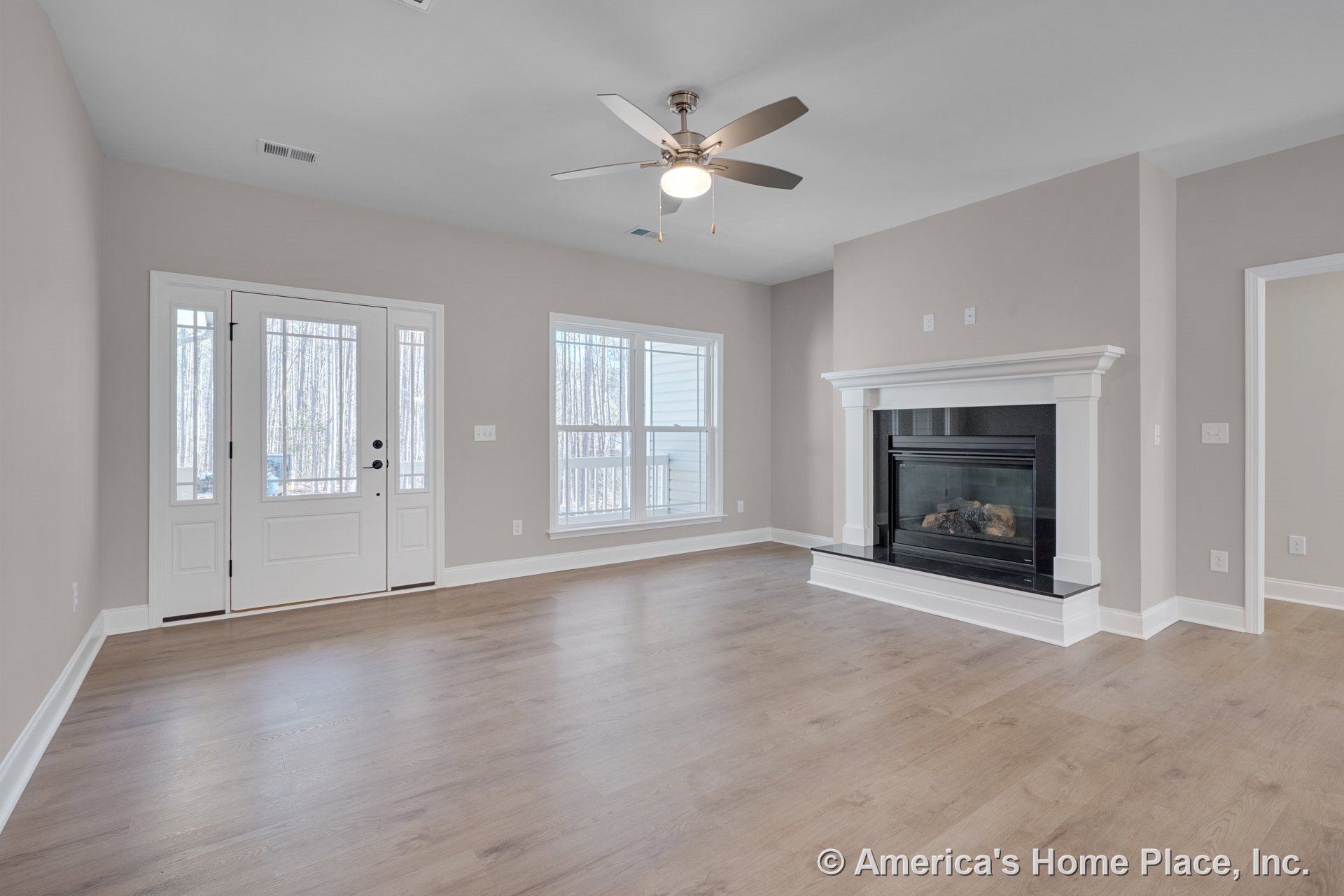 Gas fireplace with white mantel and trim, expansive front windows, light wood plank flooring, ceiling fan with integrated light, white front door featuring glass panels, neutral