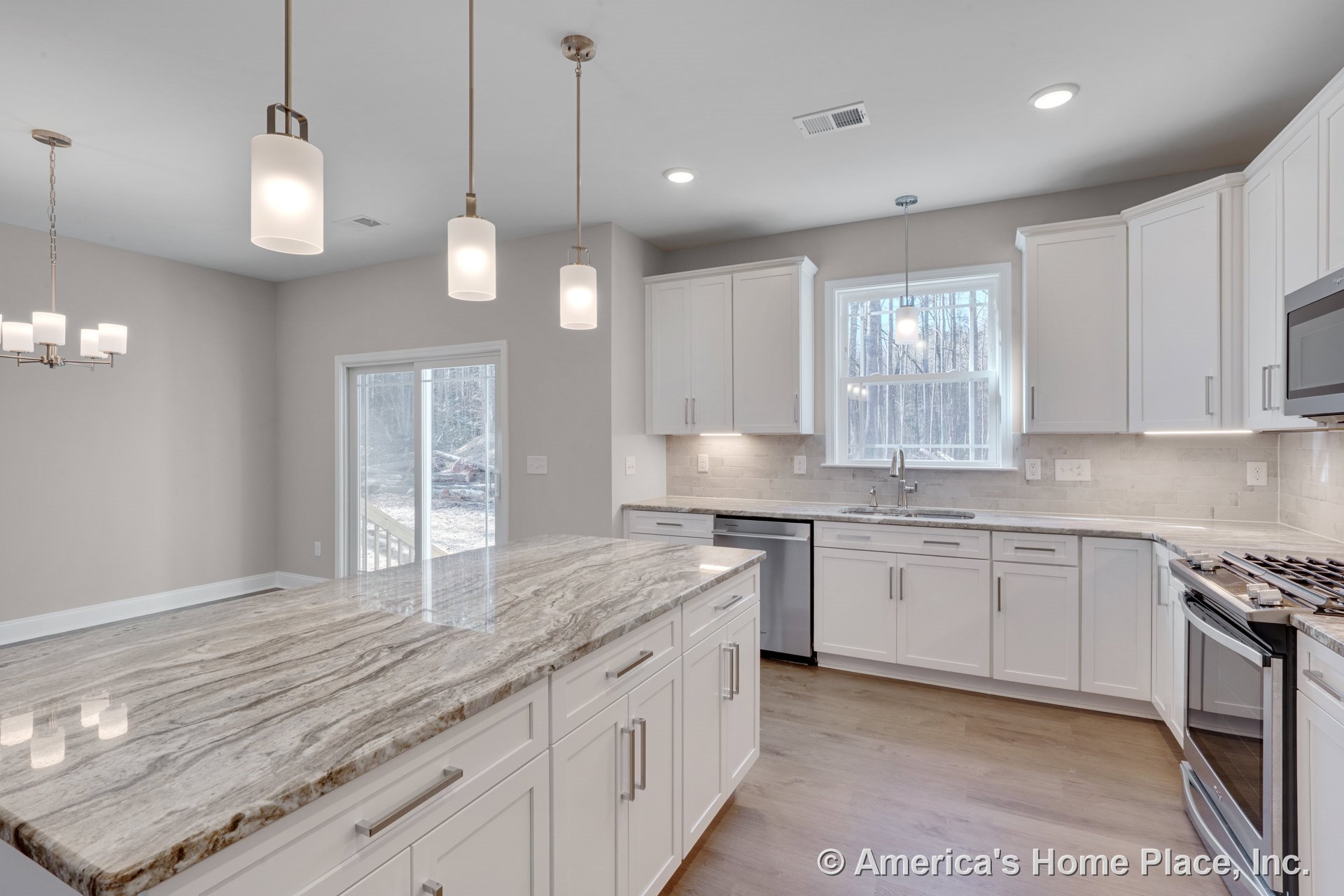 Spacious kitchen with large stone-topped island, white shaker cabinets, stainless steel oven and dishwasher, tile backsplash, wood flooring, pendant and recessed lighting, window