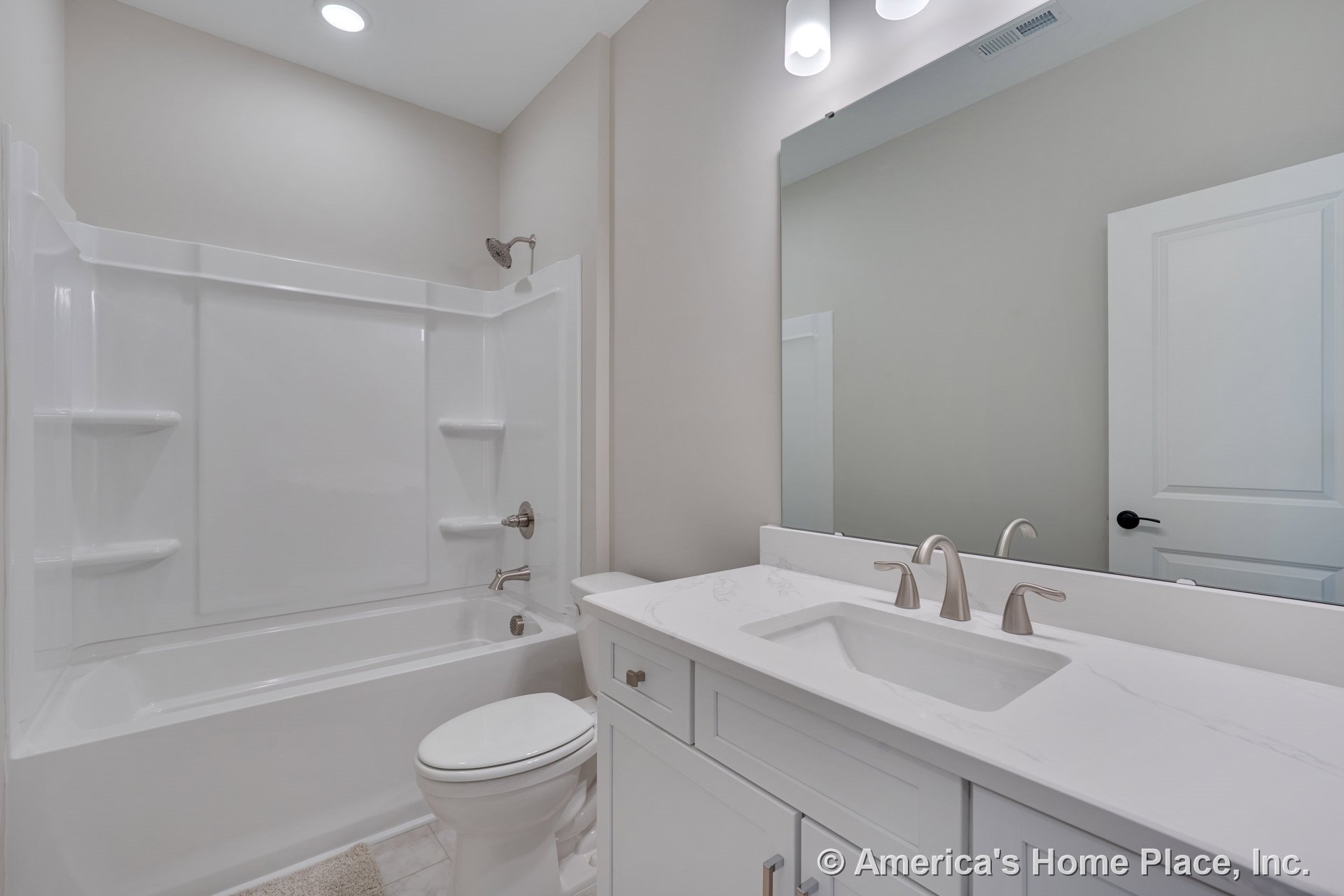 Built-in tub and shower combo with integrated shelving, white shaker vanity cabinetry topped with marble-look solid surface countertop, brushed nickel fixtures, large wall mirror