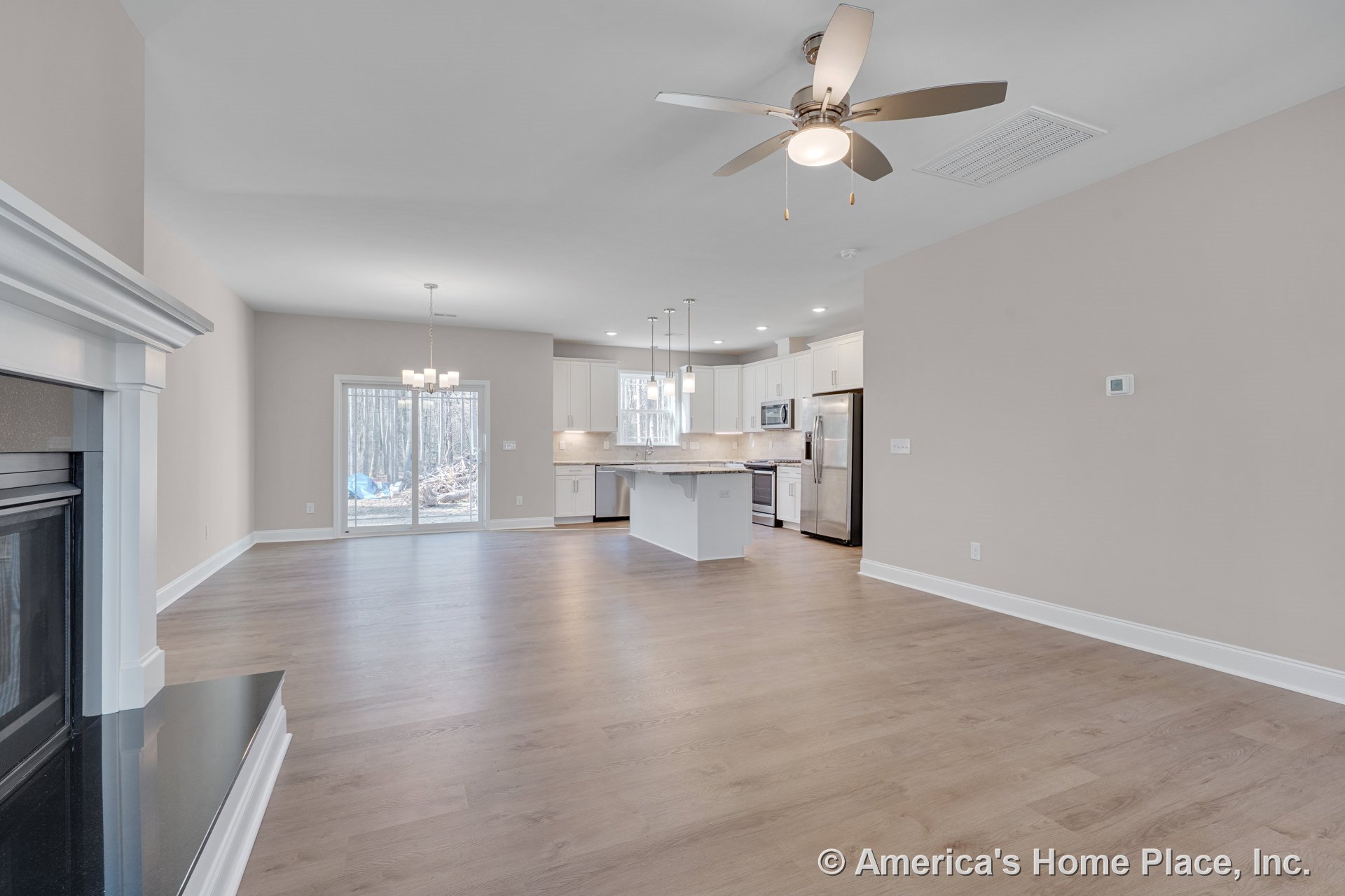 Open-concept living area with wood-look flooring, fireplace with white mantel, kitchen featuring white cabinetry, stainless steel appliances, central island with pendant lights