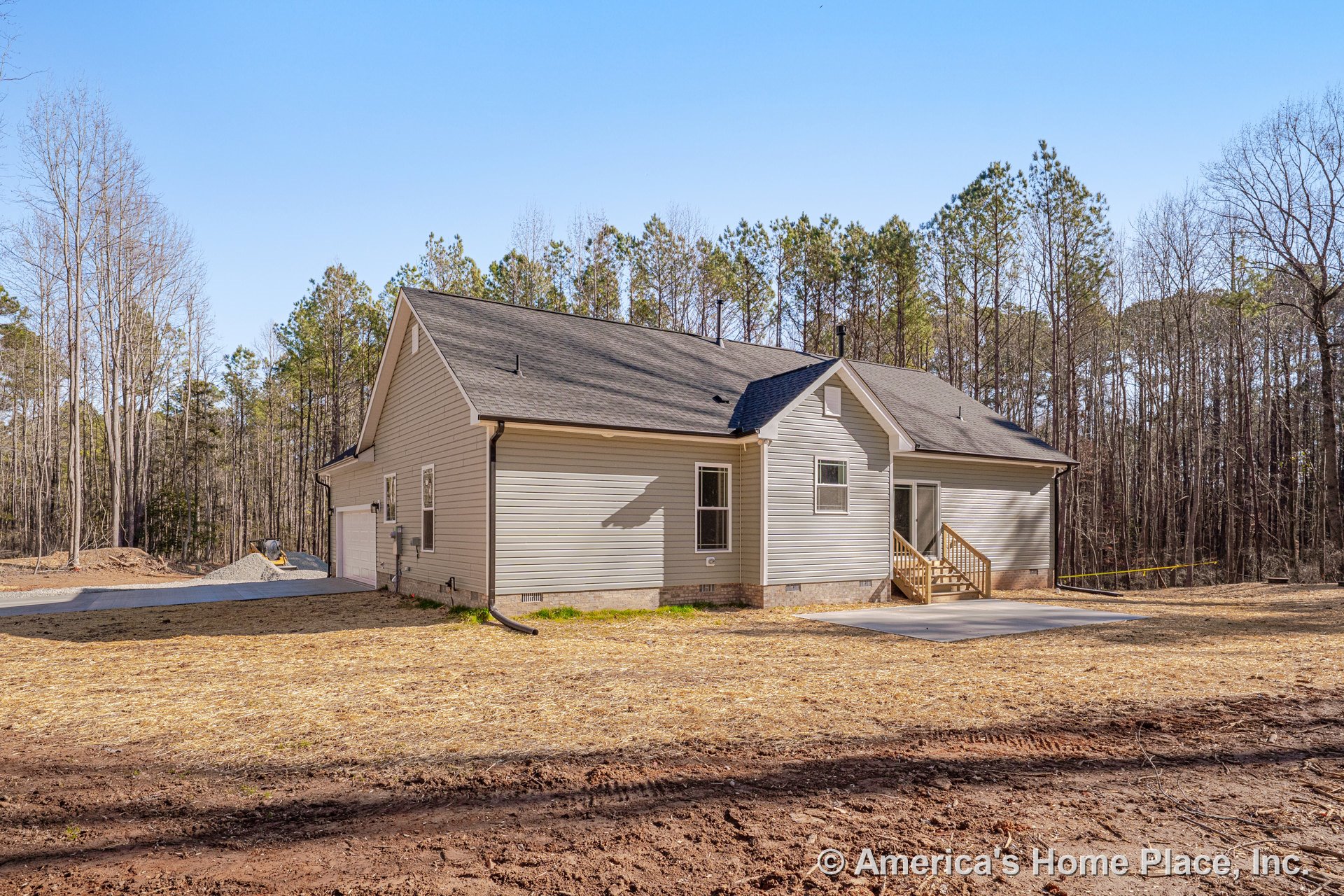 Light vinyl siding exterior with gabled asphalt shingle roof, wooden entry porch and steps, concrete patio, double-hung windows with white trim, attached garage, and downspout in a