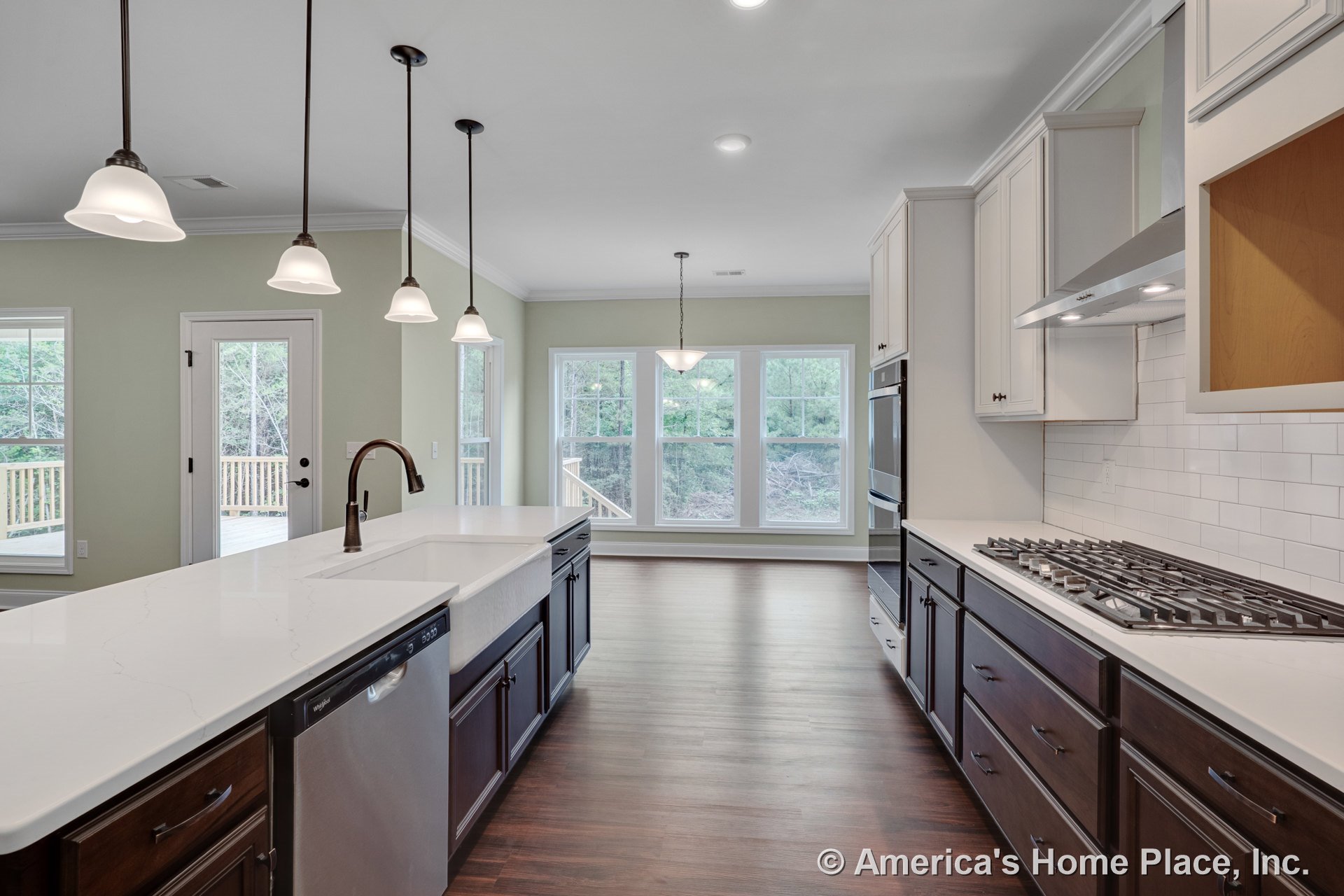 Large kitchen island with farmhouse sink and white quartz countertops, dark wood lower cabinets, white upper cabinets, subway tile backsplash, double wall ovens, pendant lights