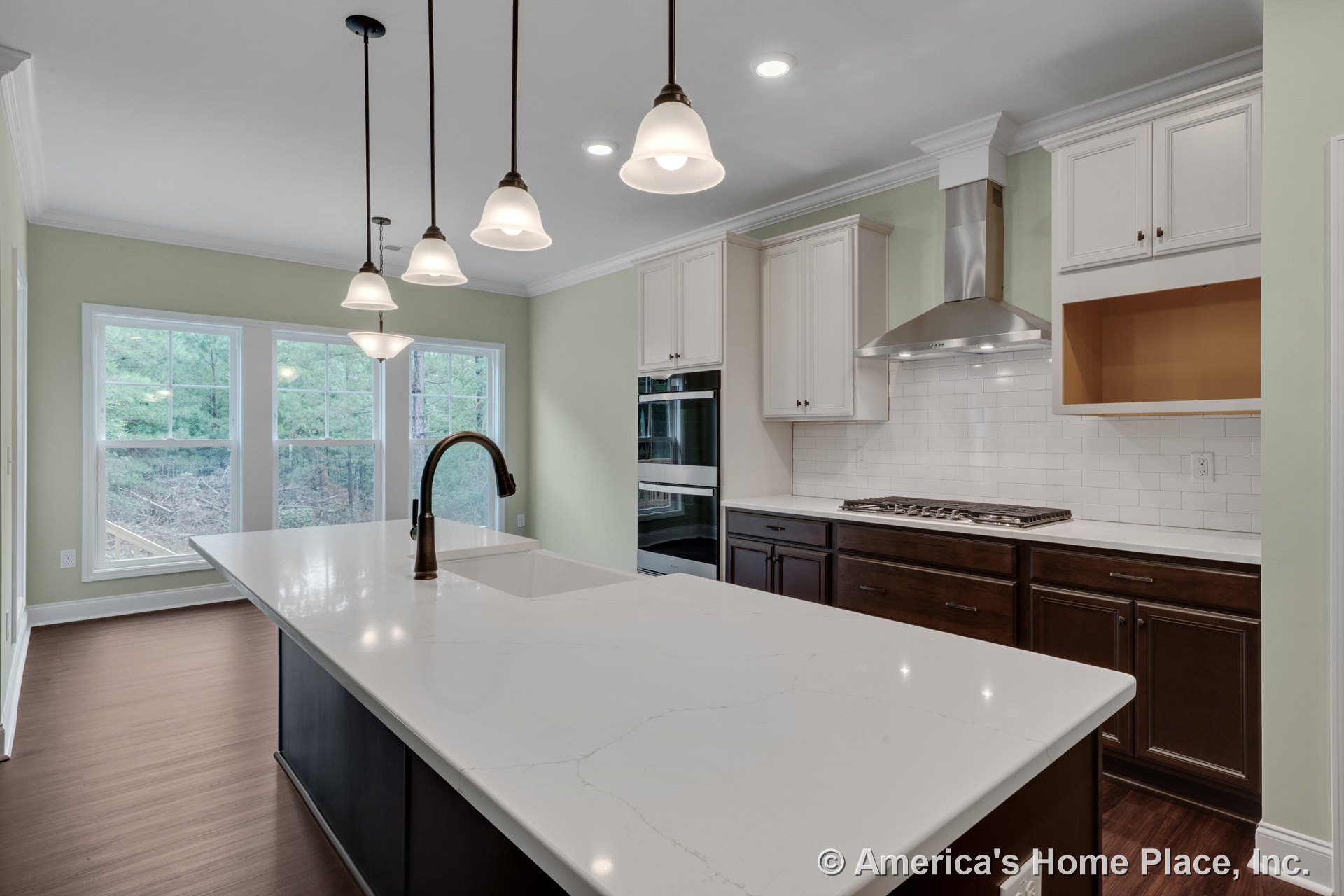 Spacious kitchen with white quartz countertops, dark wood lower cabinets, white upper cabinets, subway tile backsplash, large island with built-in sink, pendant lights, stainless
