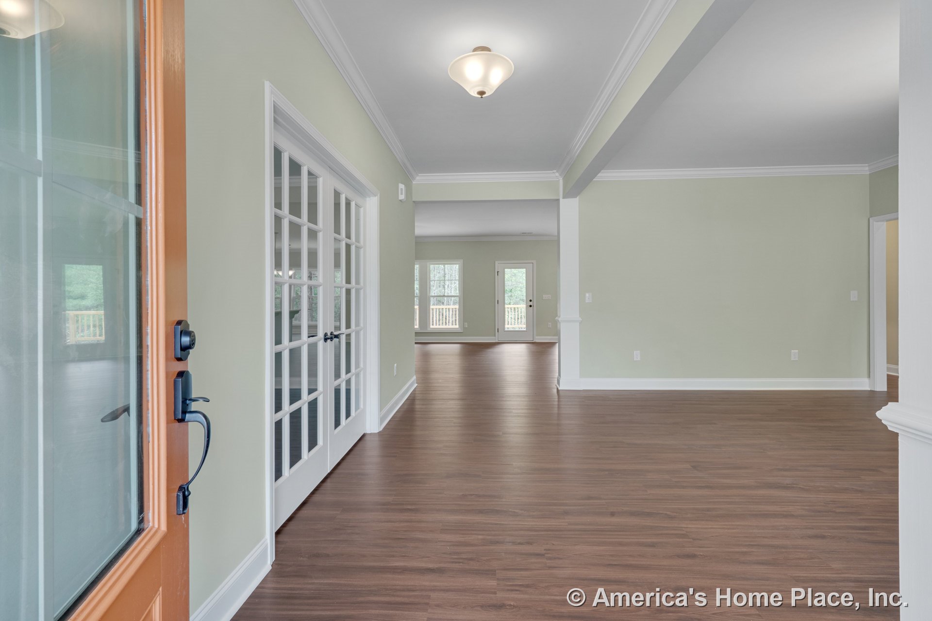 Foyer with wood-look flooring, glass front door, French doors with white trim, crown molding, ceiling light fixture, transom window, and large rear windows in an open layout.