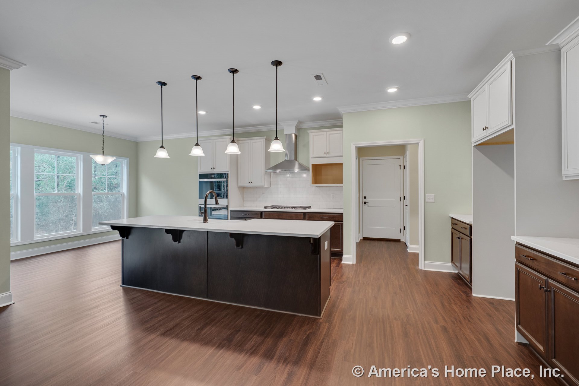 Spacious kitchen with large dark cabinetry island, white countertops, multiple pendant lights, white upper cabinets, stainless steel range hood, tile backsplash, wood-look