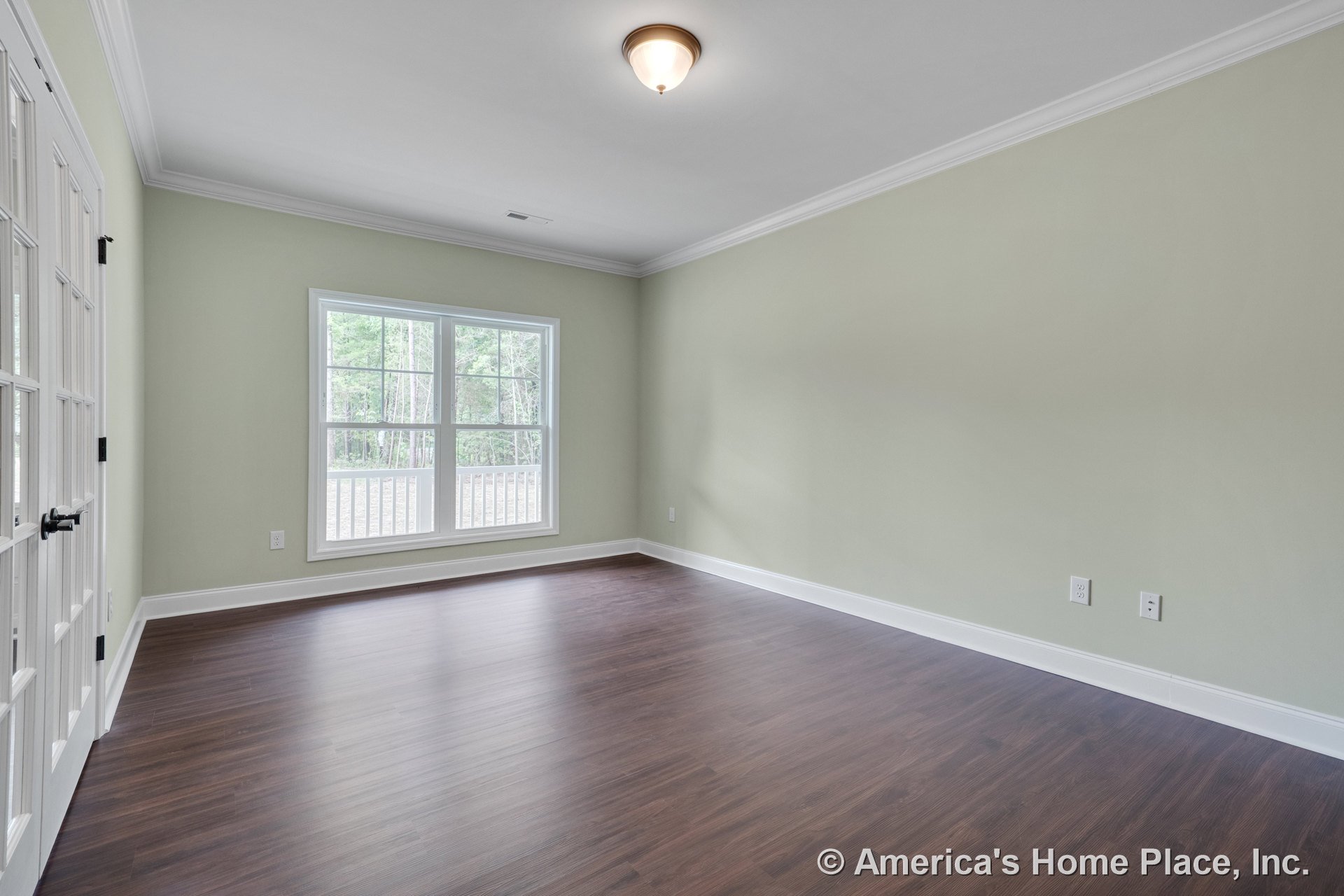 Spacious living room with double French doors, large picture window, crown molding and baseboard trim, flush mount ceiling light, wood-look plank flooring, and light green painted