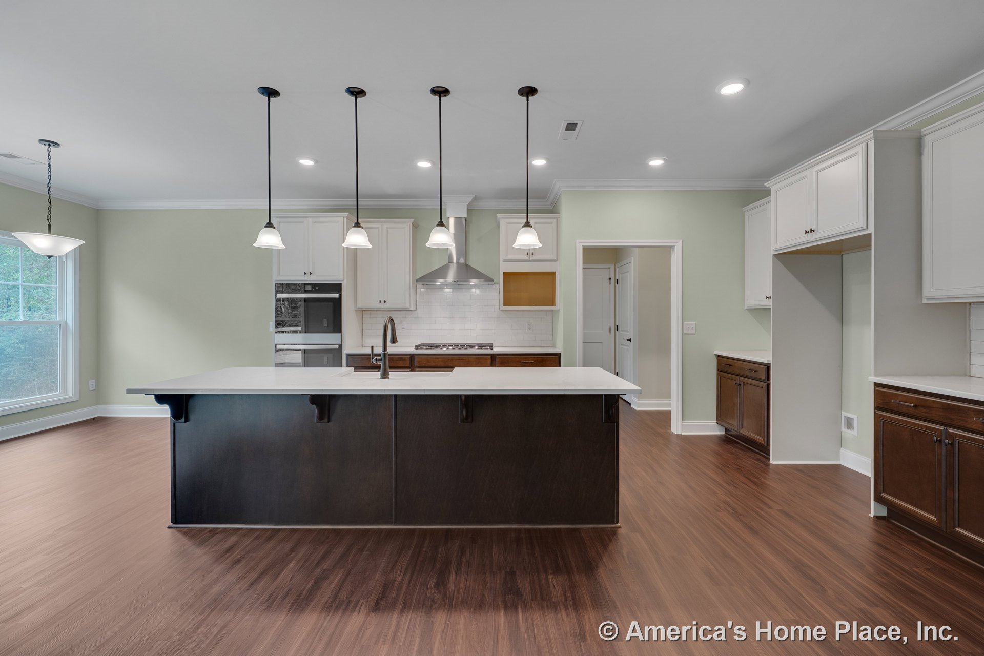 Large kitchen island with dark wood base and quartz countertop, white upper cabinets, stainless steel range hood, double wall ovens, pendant lights above island, tile backsplash