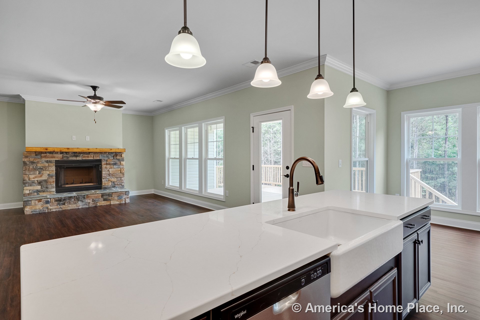 Stone fireplace with wood mantel, expansive window wall, white quartz kitchen island with farmhouse sink and bronze faucet, dark wood cabinetry, pendant lights above island, wood