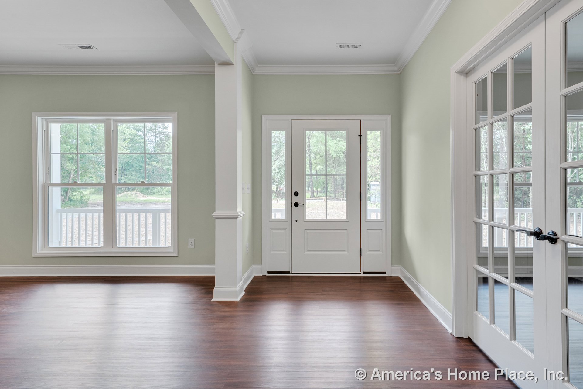 White front door with glass sidelights, double French doors with glass panes, expansive windows with white trim, wood plank flooring, crown molding, baseboards, and open interior